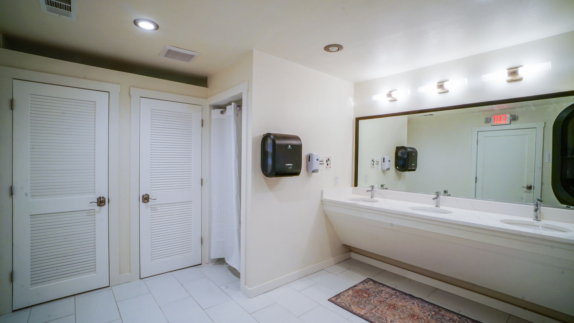 Public restroom with white walls, sinks, mirrors, and stalls with closed doors.
