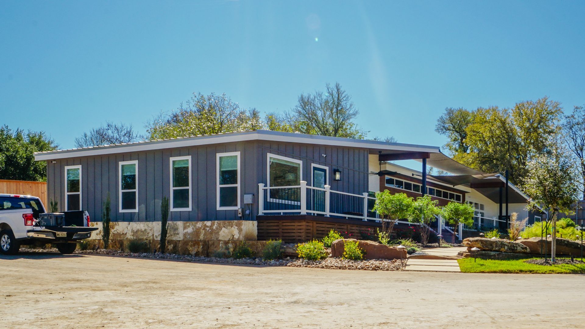Gray building with large windows and a covered patio under a blue sky, with a white truck parked nearby.