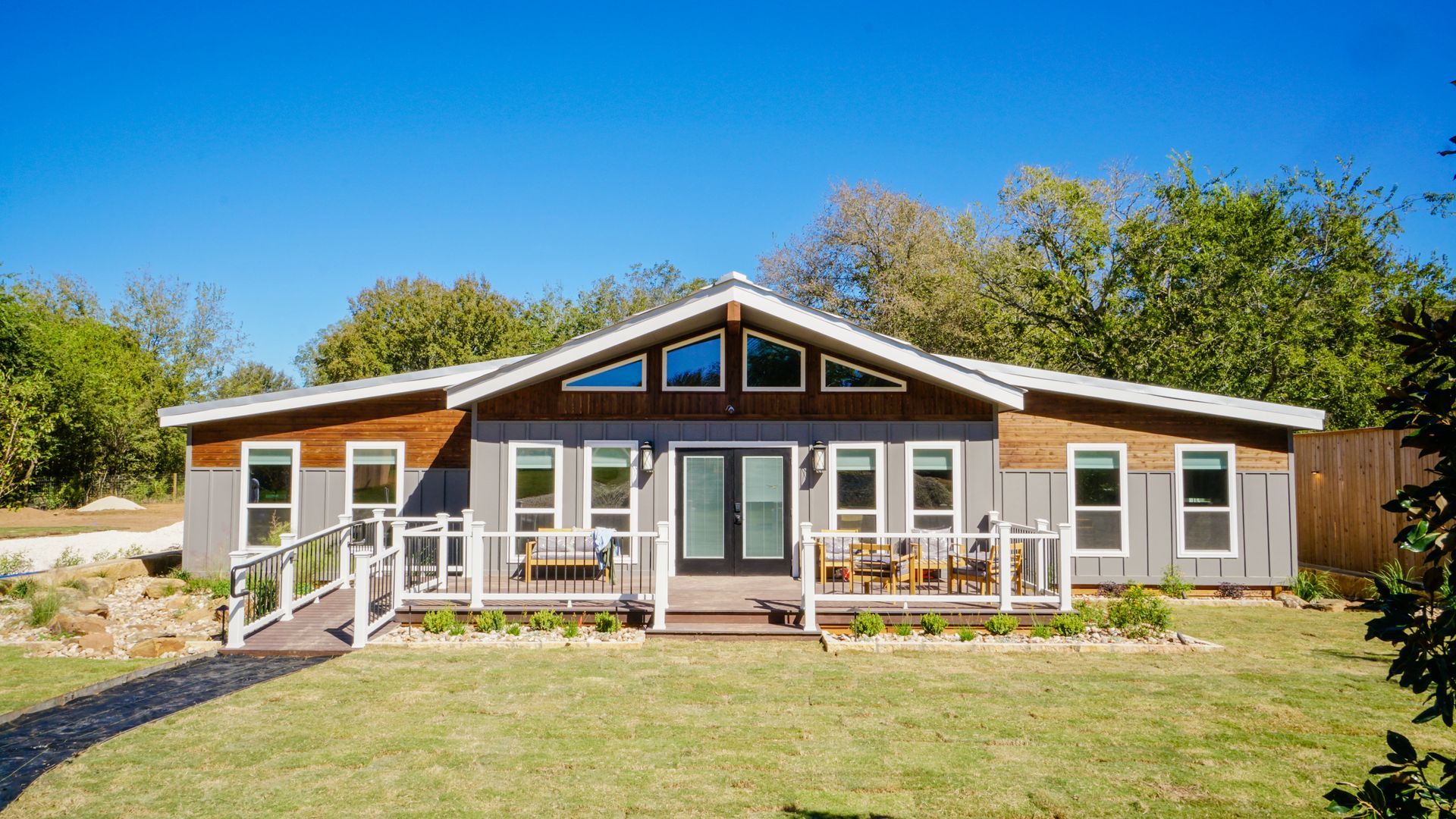 Modern single-story house with gray and wood siding, a porch, and a lush green lawn on a sunny day.