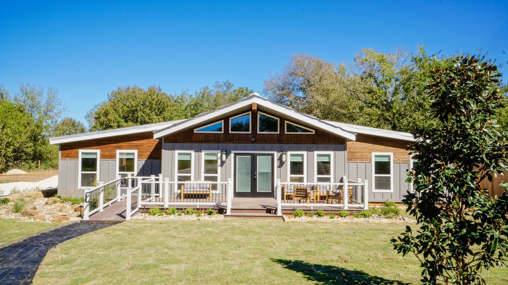 Gray house with wood accents, large windows, and a front porch on a sunny day.