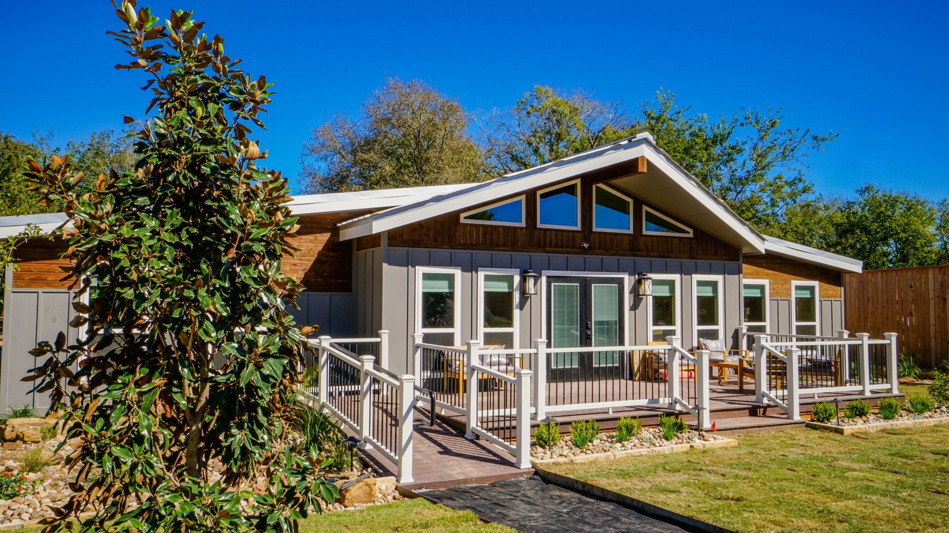 A modern, single-story house with a wooden deck and a sloping roof against a blue sky.