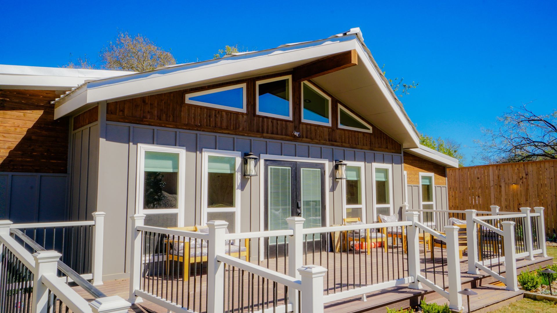 Home exterior with a gray and brown facade, deck, and blue sky.