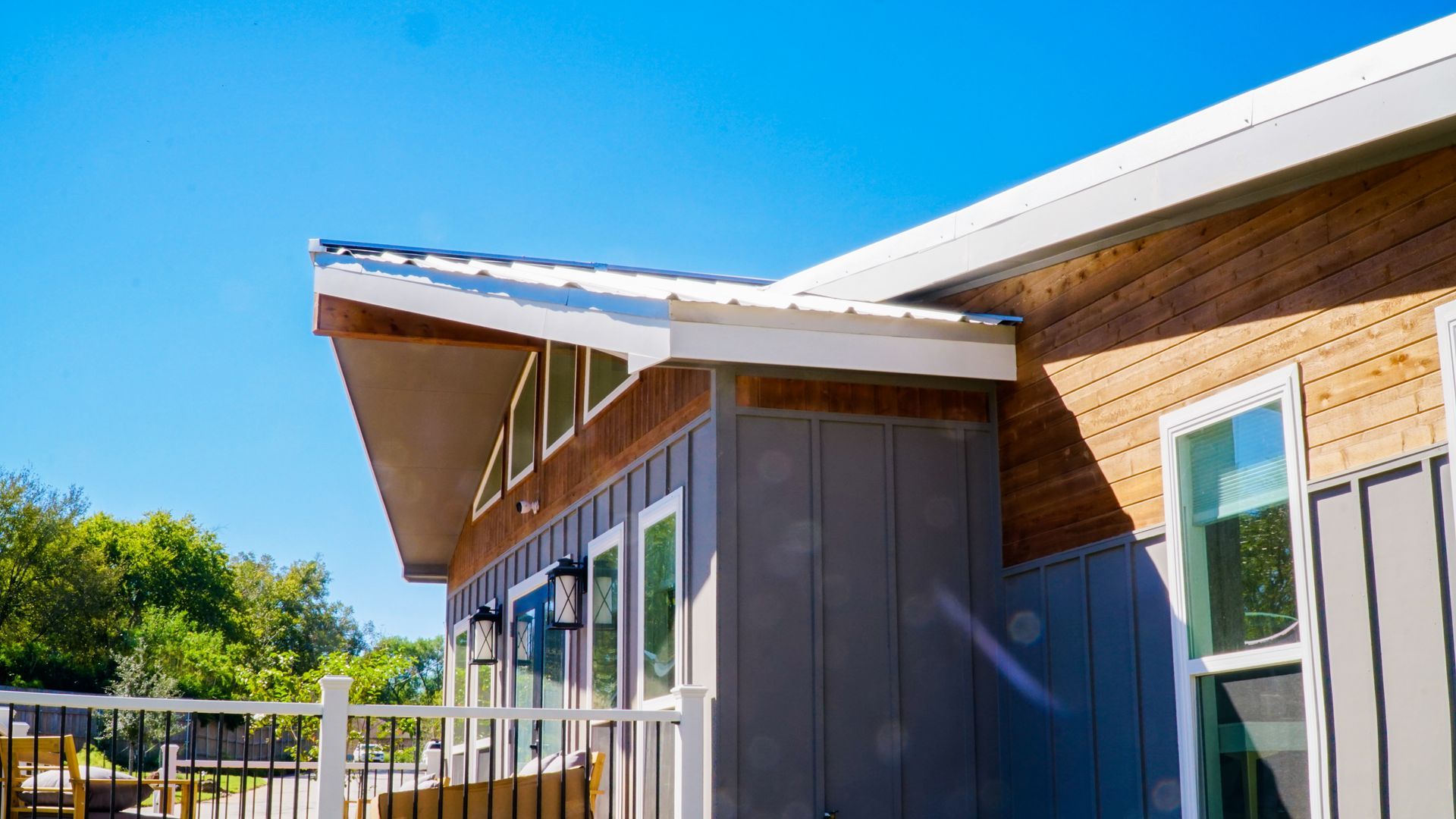Modern home exterior with gray and wood siding, white trim, and a blue sky.