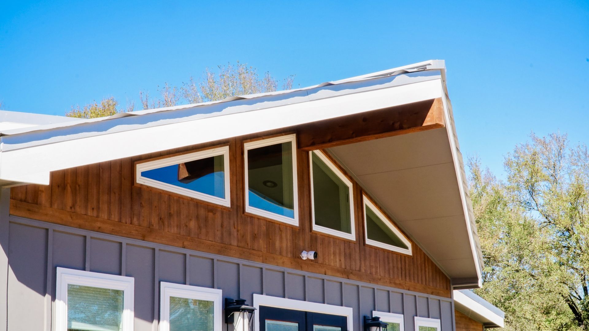 Modern house with triangular windows under a light roof, with blue sky.