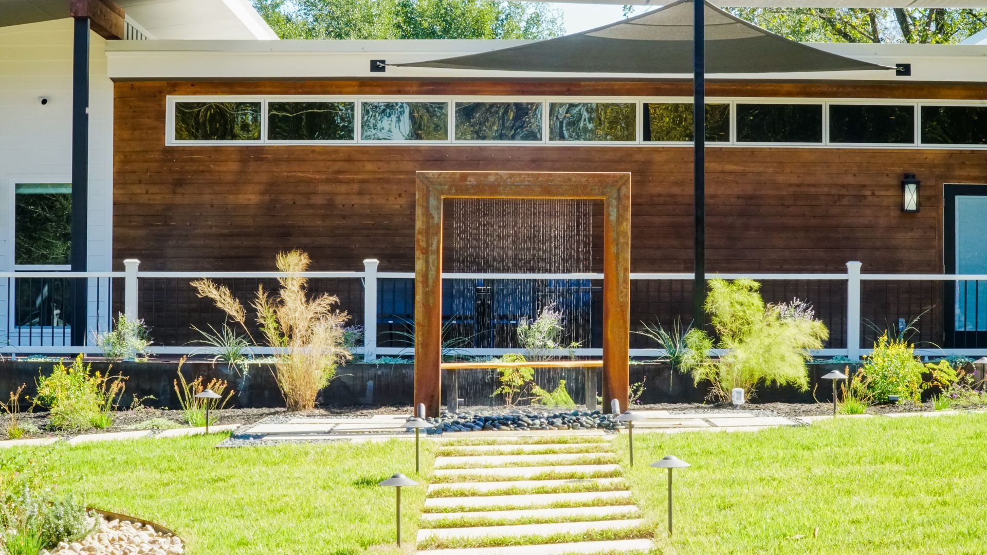 A modern home with a water feature in front of a wood-paneled wall, set on a grassy lawn.