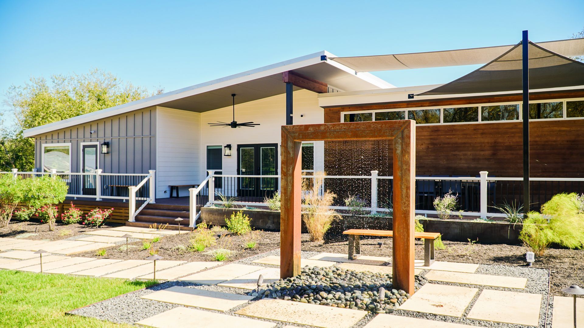 Modern house exterior with water feature, patio, and landscaping under a sunny sky.