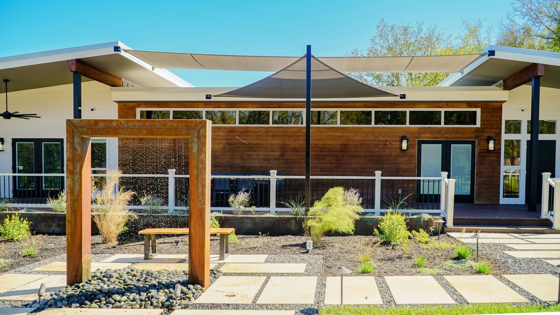 Modern home exterior with wooden siding, a water feature, and a shaded patio.