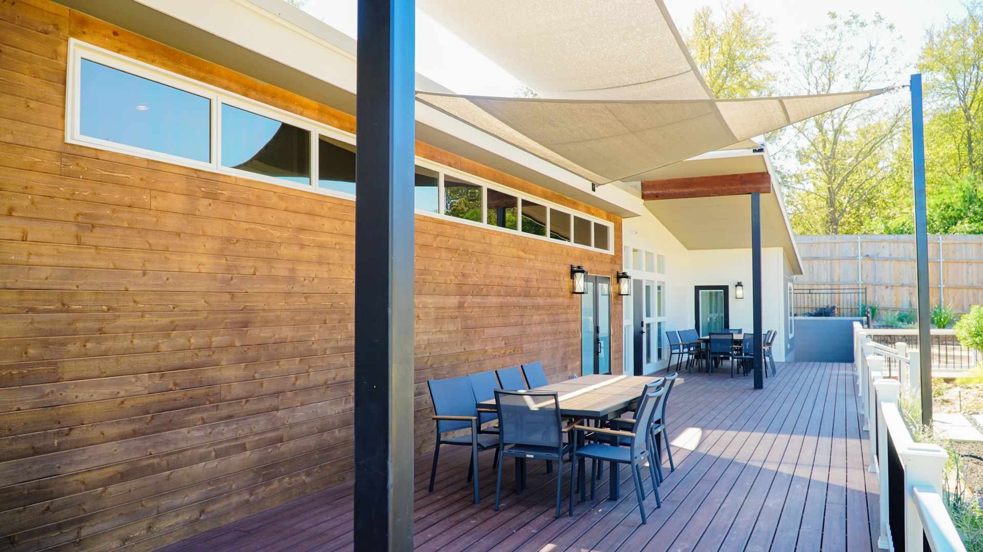 Exterior deck with a wooden facade, dining table, and shade sail.