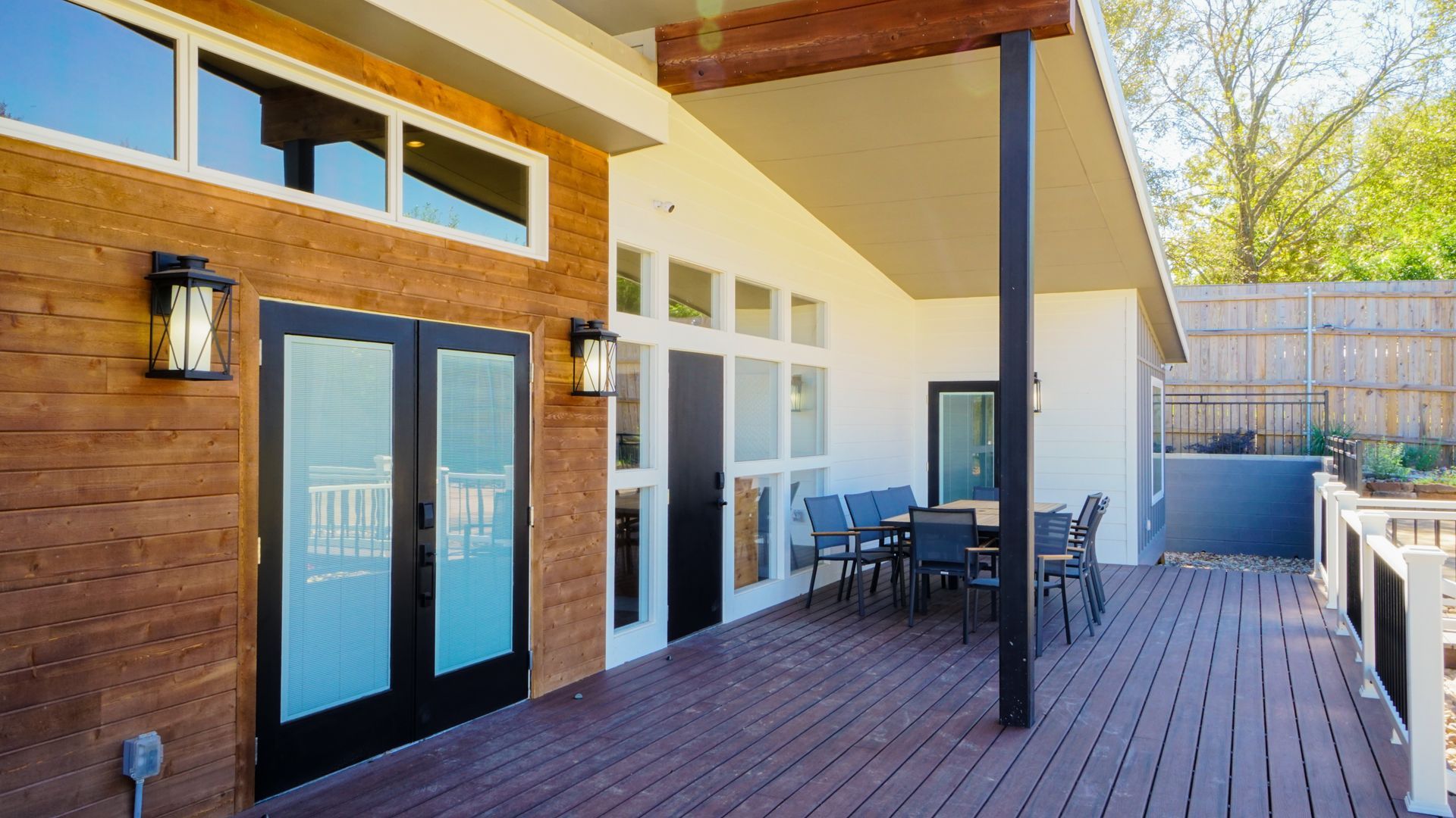 Exterior view of a modern home with a wooden deck, patio furniture, and glass doors.