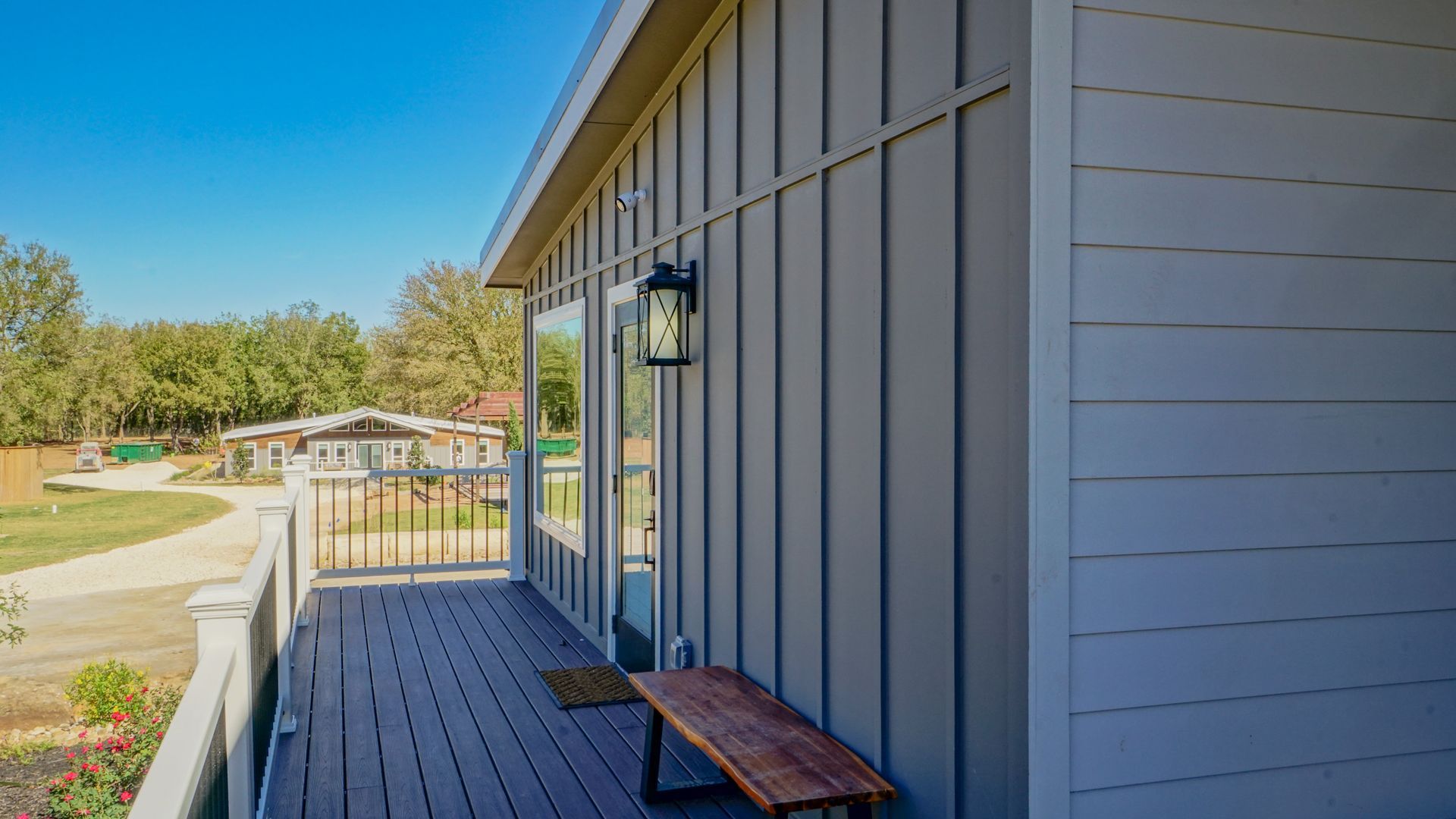 Exterior of a house with a gray vertical-paneled wall, deck, bench, and a view of a road and other buildings.
