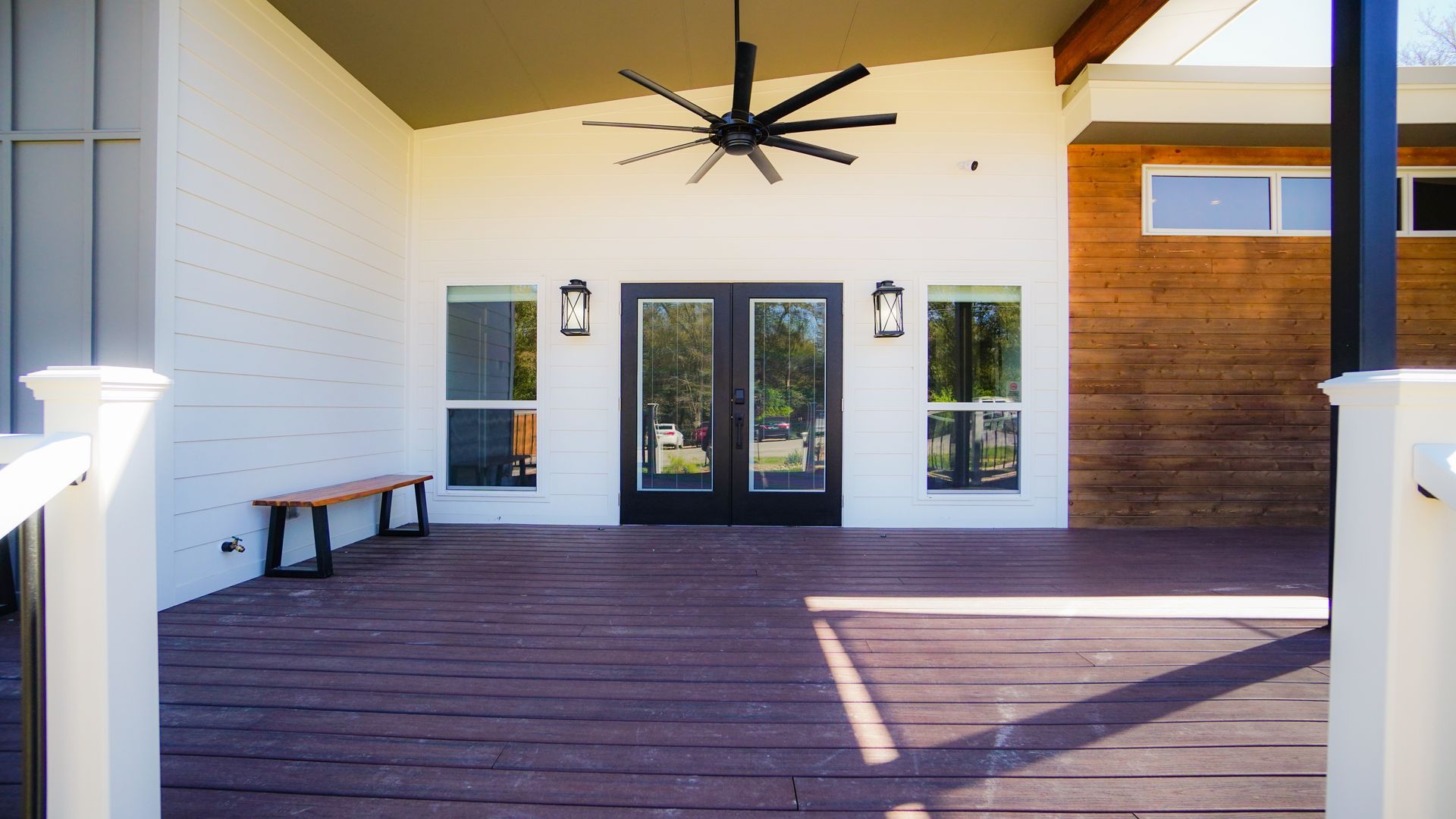 Covered porch with dark wood deck, white brick, black double doors, and ceiling fan.