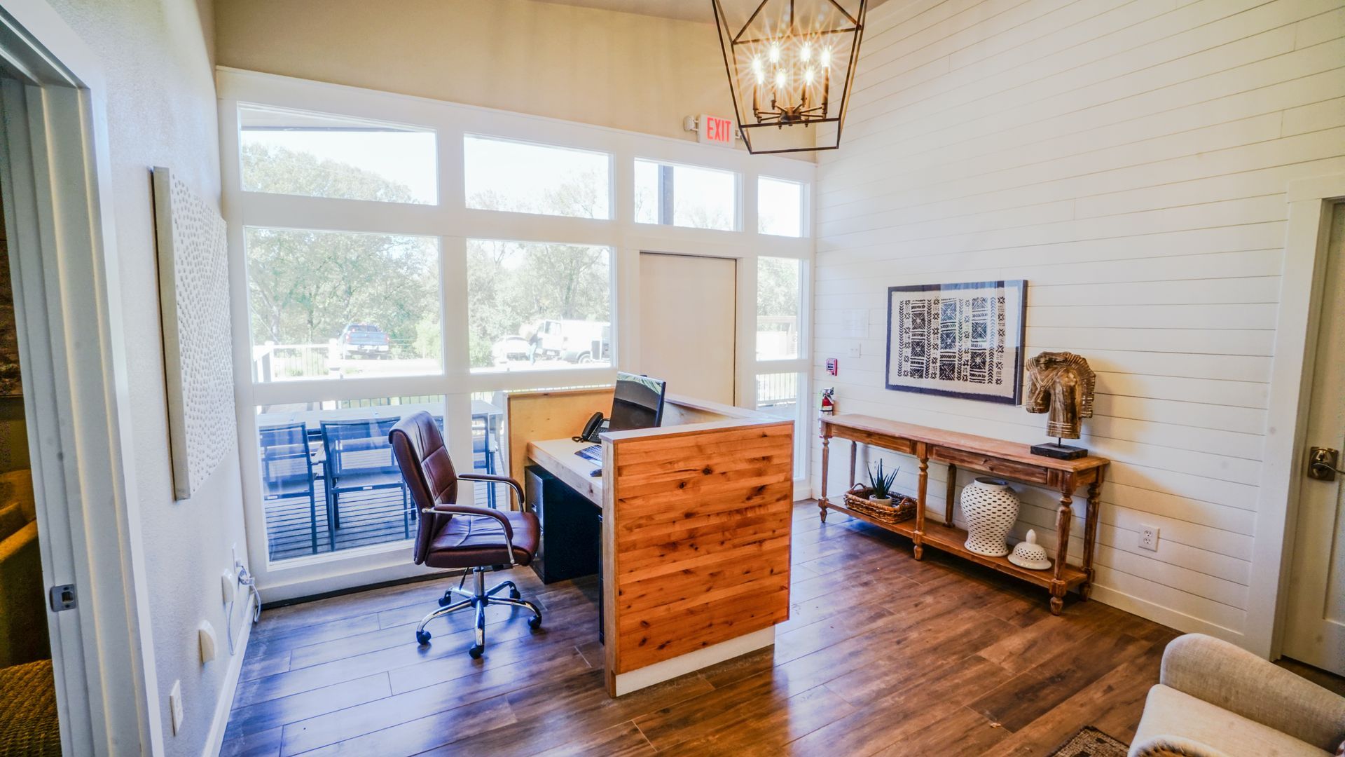 Reception area with desk, large windows, wood flooring and furniture, and decorative items.
