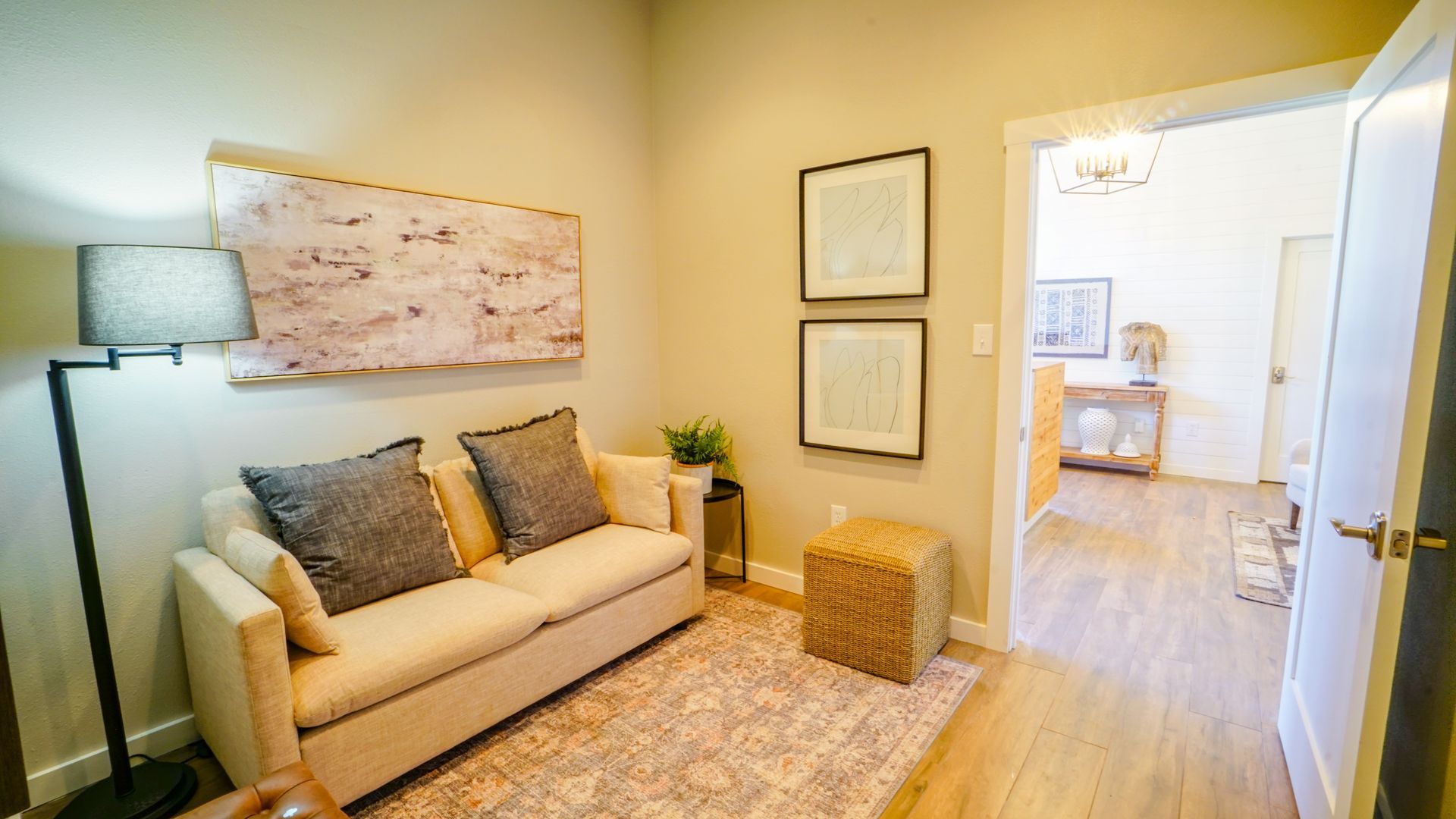 Cozy living room with cream couch, rug, artwork, and doorway leading to another room.