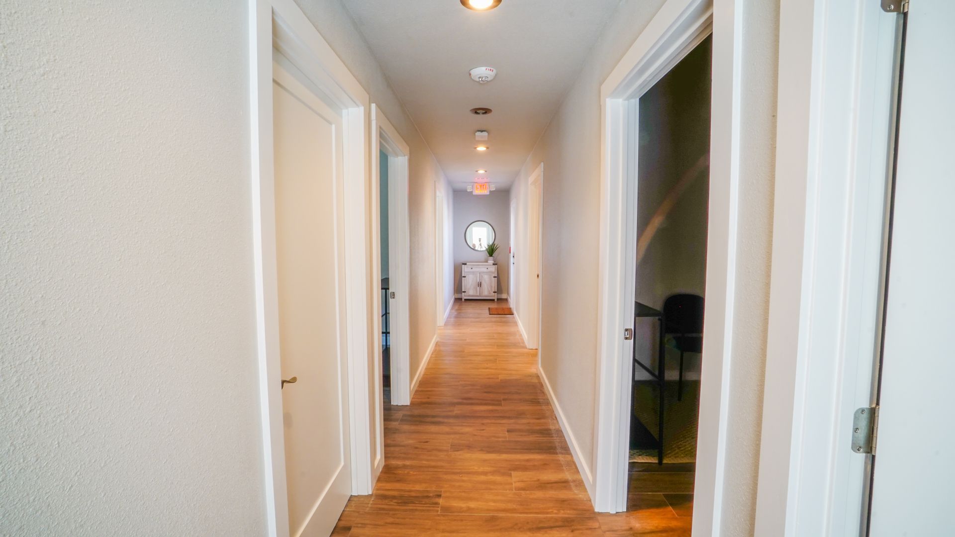 Hallway with wooden floor and white walls; doors on both sides lead to rooms.