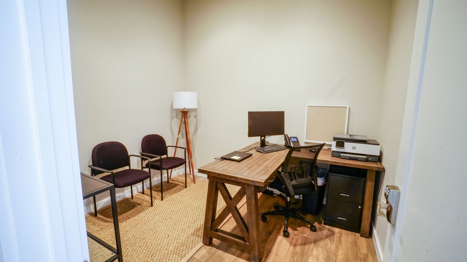Small office with desk, chairs, rug, lamp, and computer.