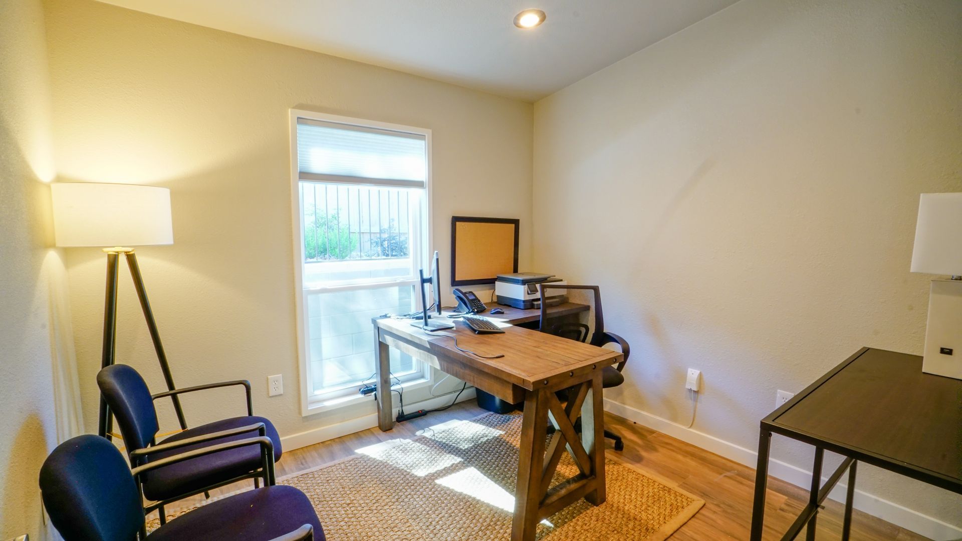 Office space with a wooden desk, chair, window, two blue chairs, and a floor lamp.
