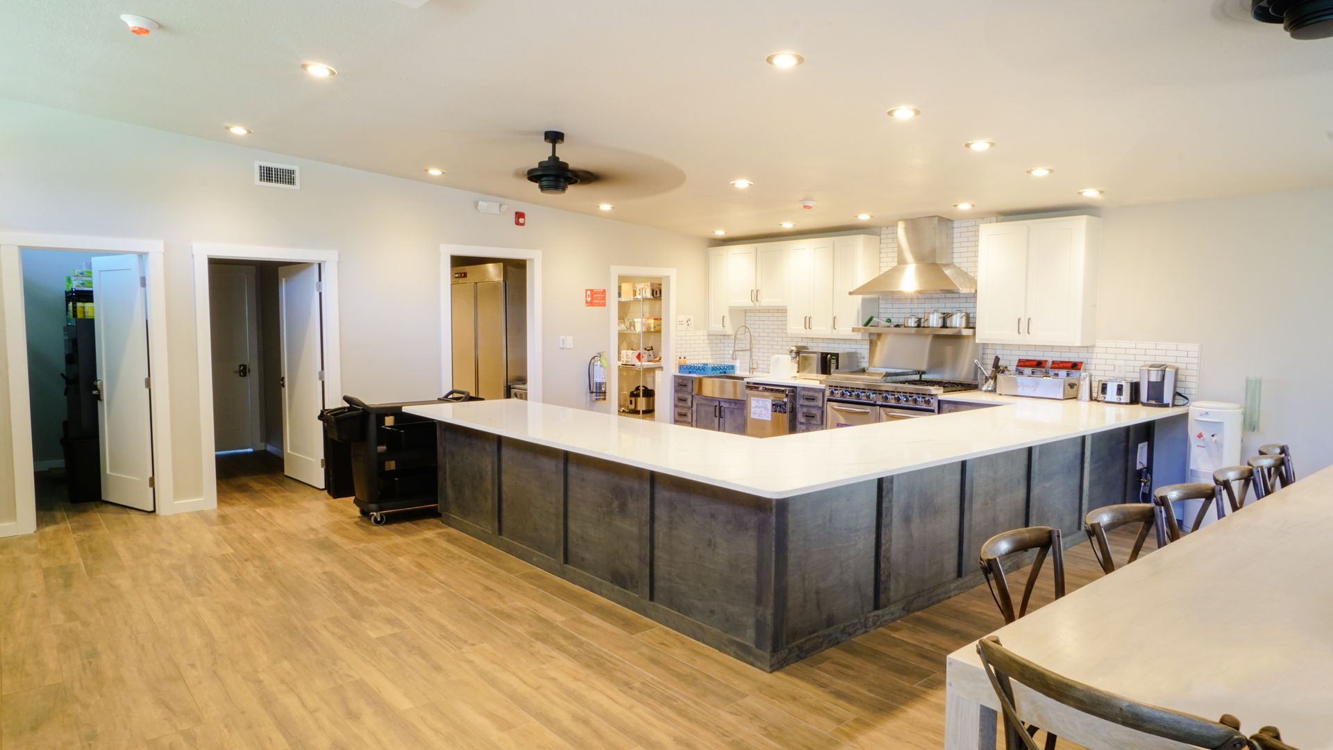 Spacious kitchen with large island, stainless steel appliances, and multiple doorways. Light wood floors and white cabinets.