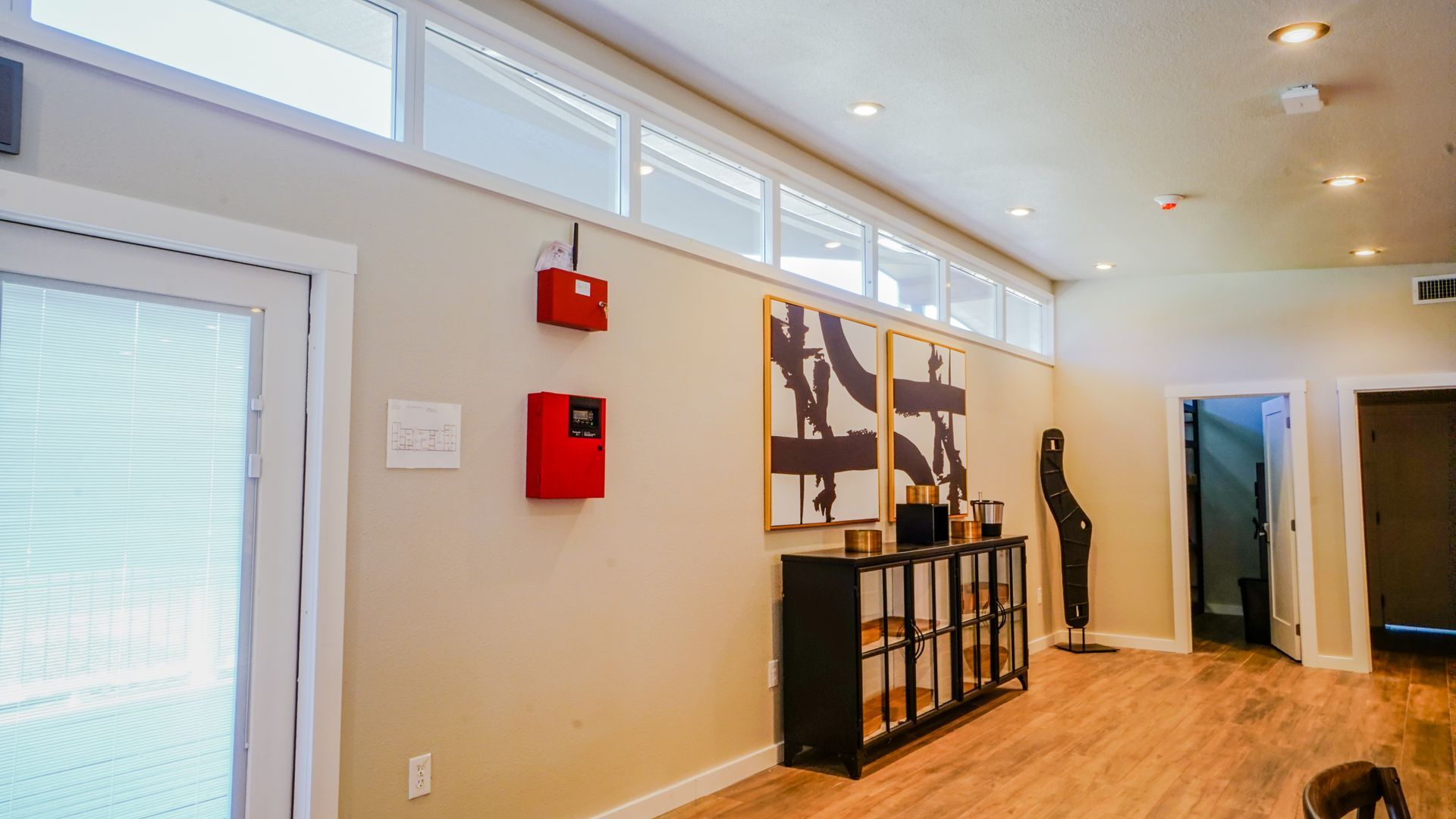 Interior view of a room with natural light from a window, beige walls, wood floor, and black furniture.