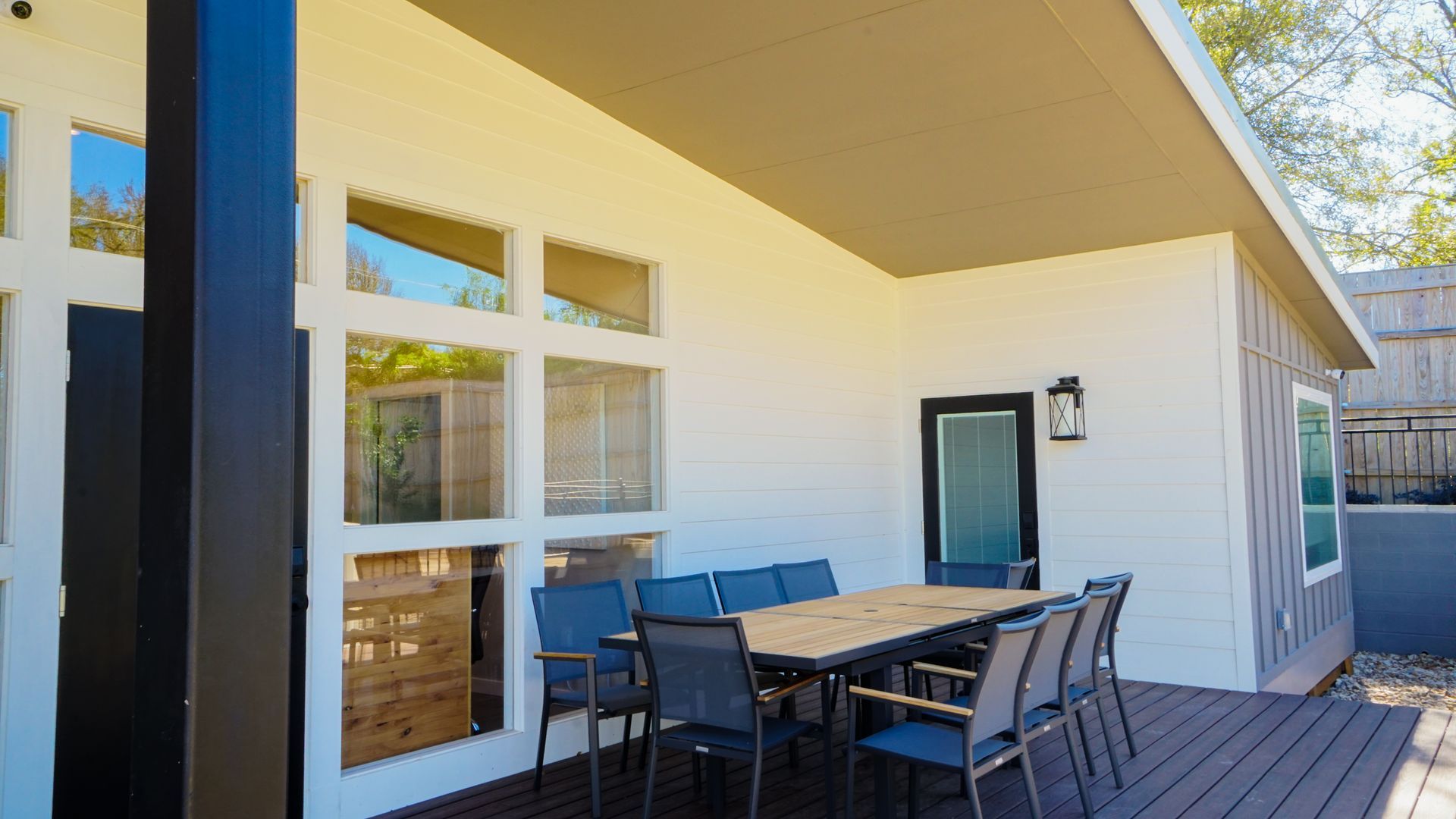 Covered patio with a table and chairs next to large windows.