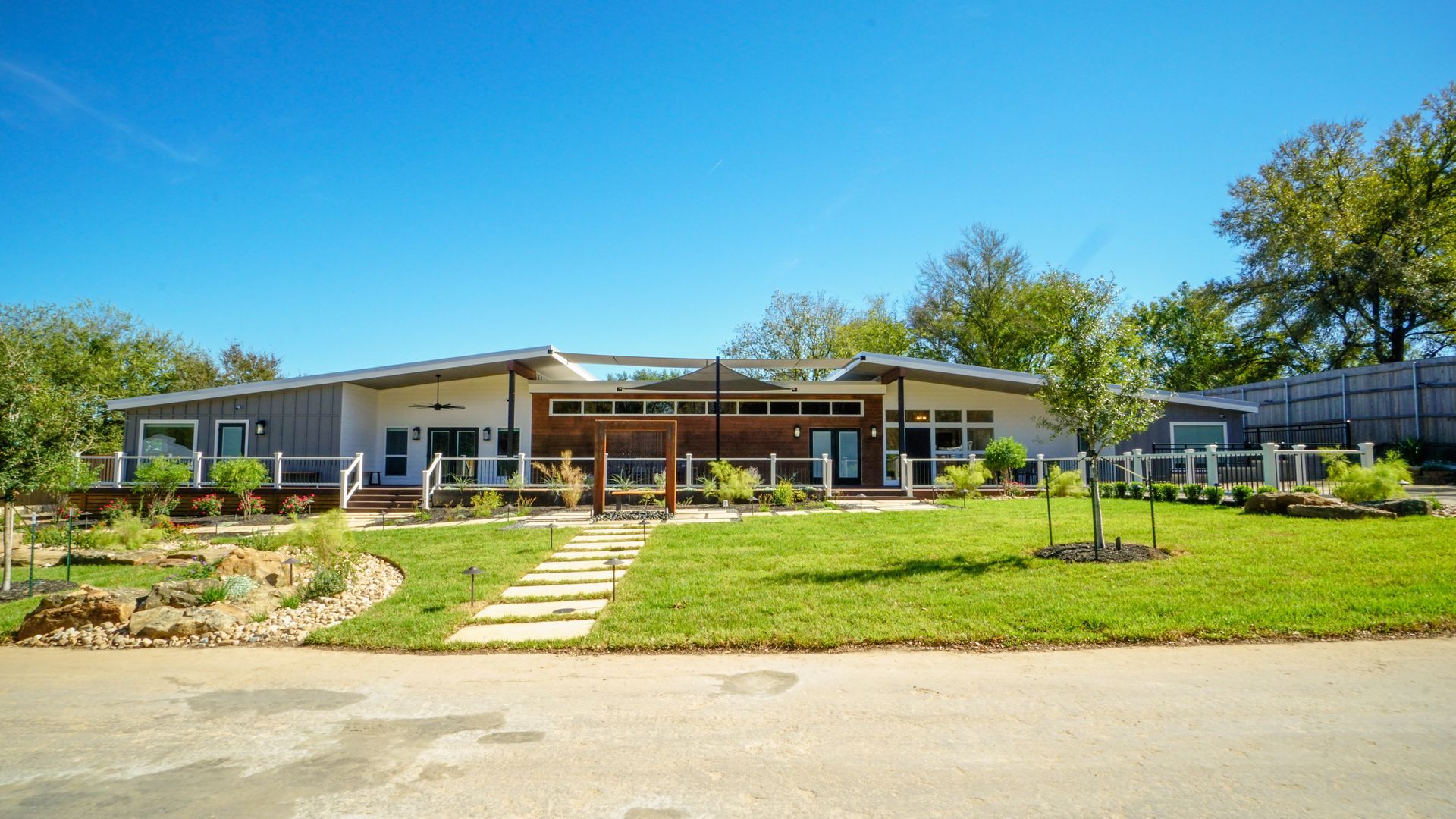 Modern ranch home with grey siding, large windows, and landscaped yard under a blue sky.