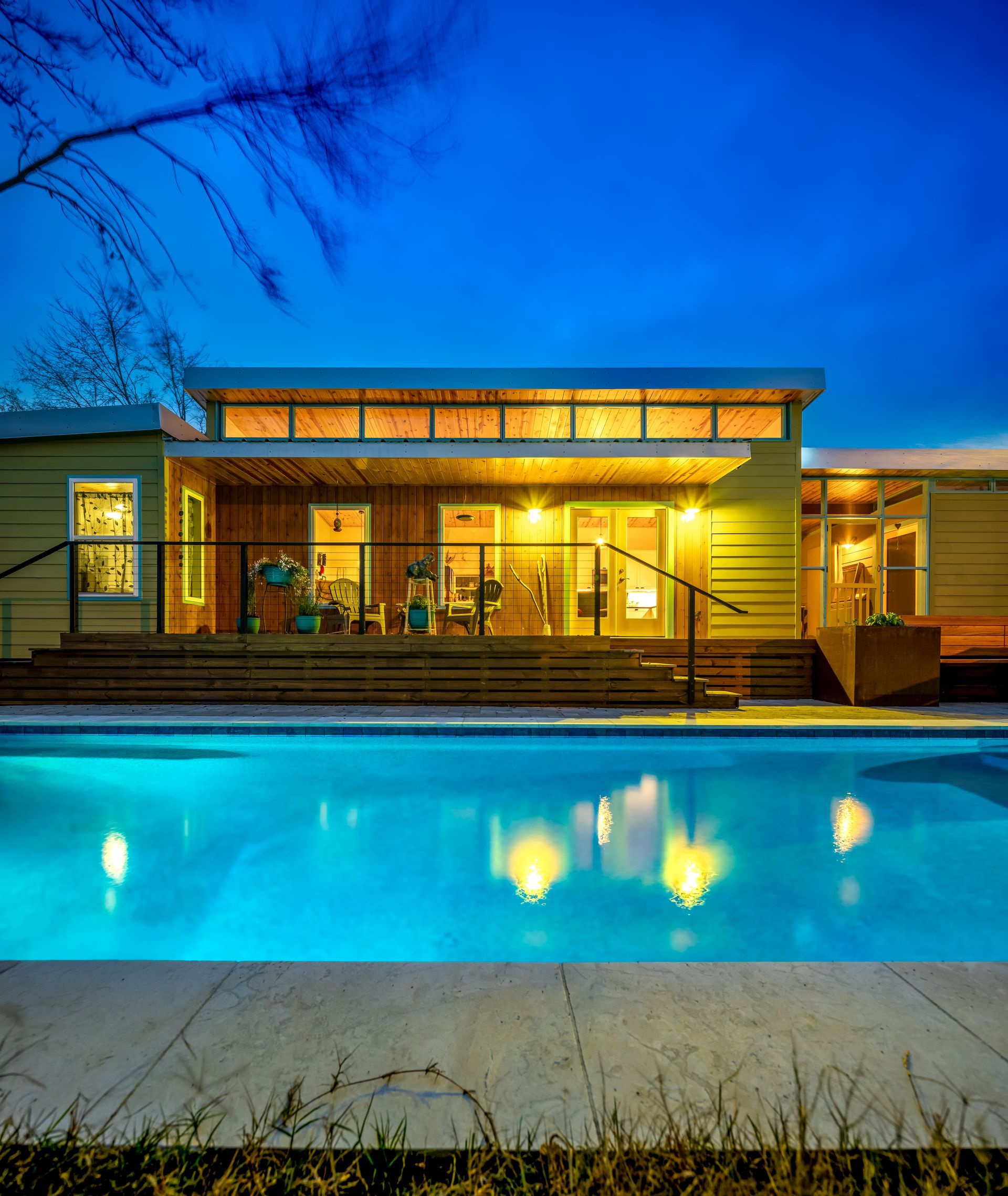 Modern house at dusk with warm lights reflecting in a blue swimming pool