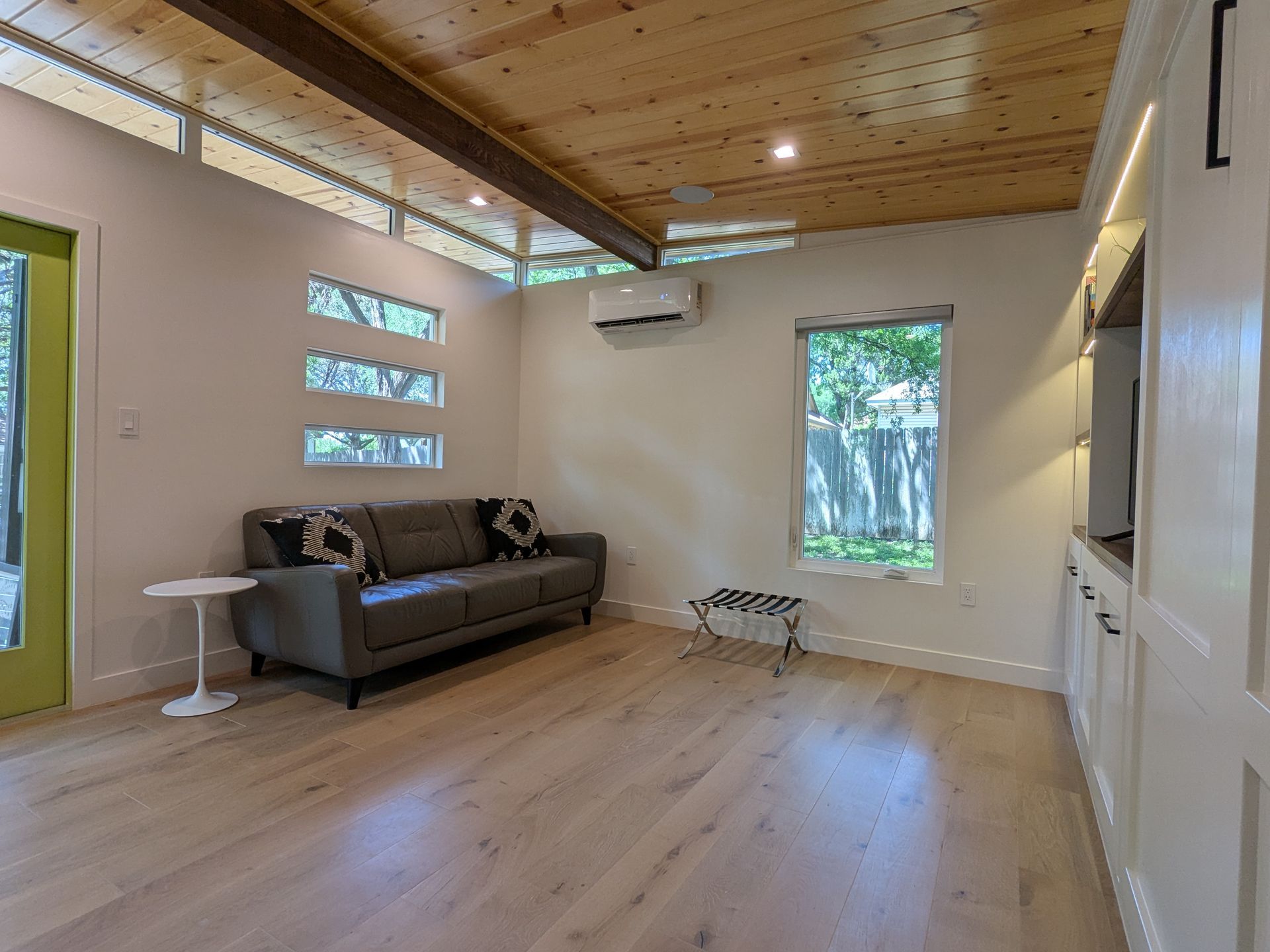 Modern living room with wood floors, gray couch, white walls, and a wood ceiling.