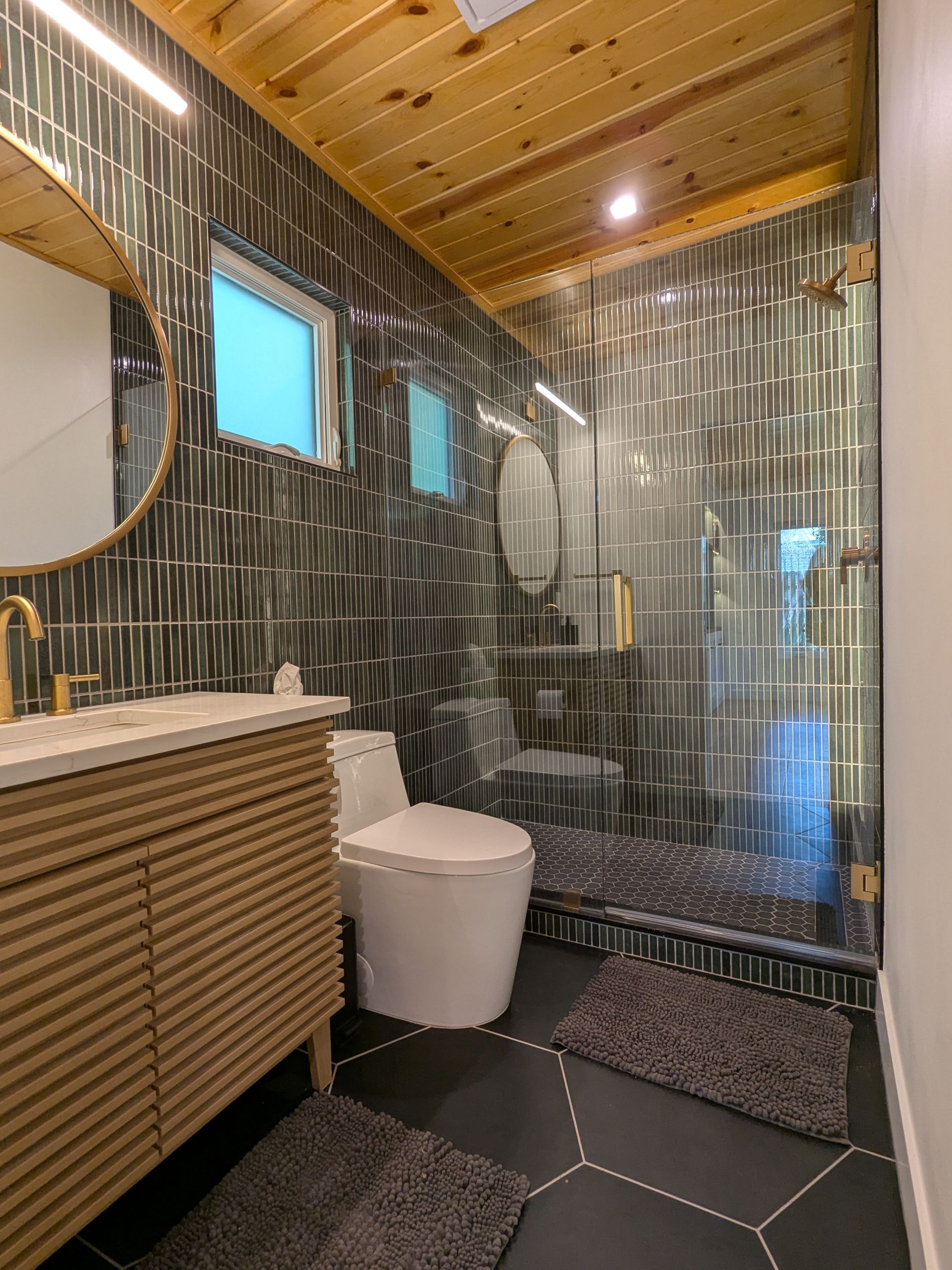 Modern bathroom with dark tile, wood vanity, and a glass shower.