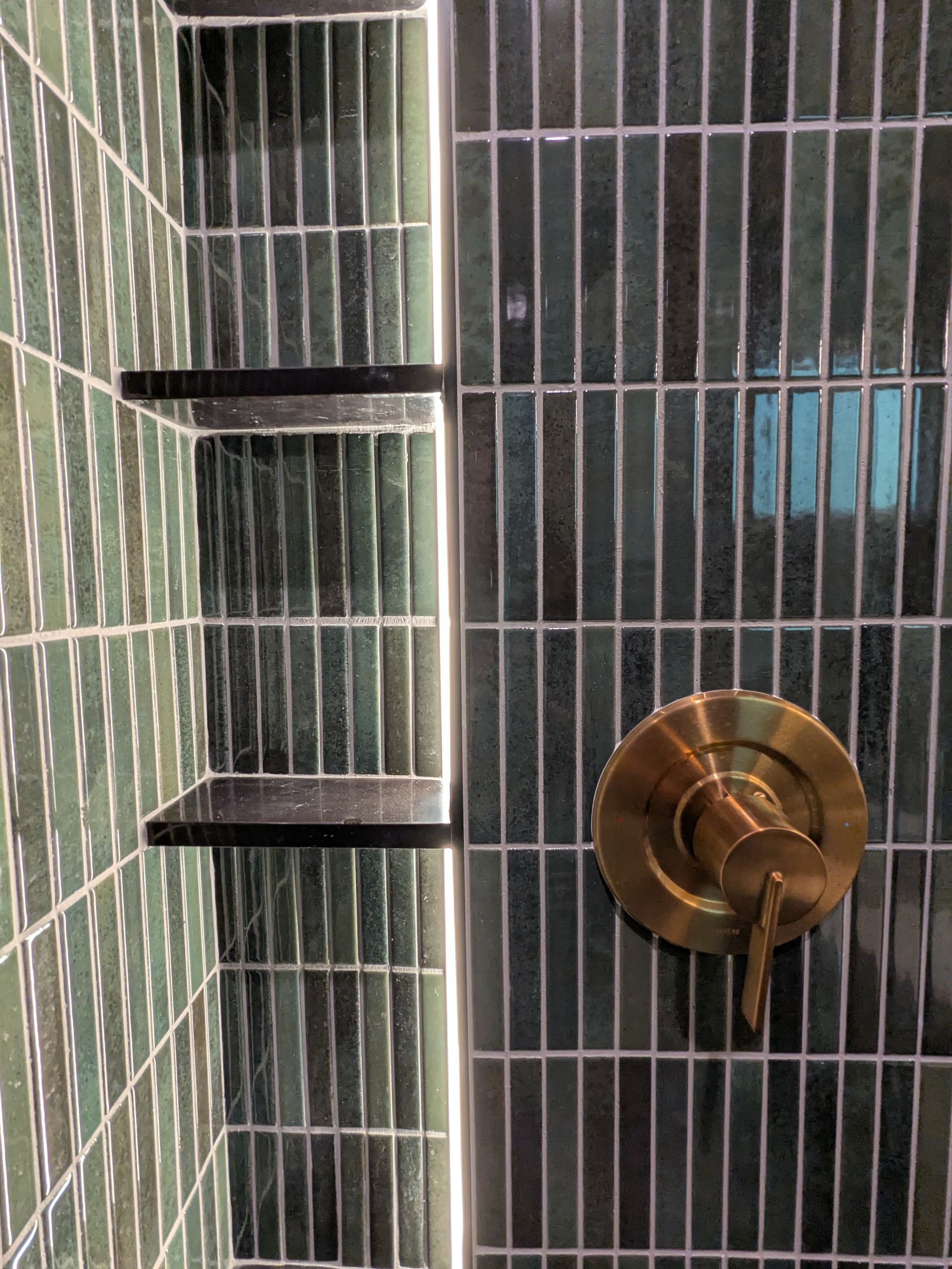 Green tiled shower with two built-in shelves and gold-colored faucet.