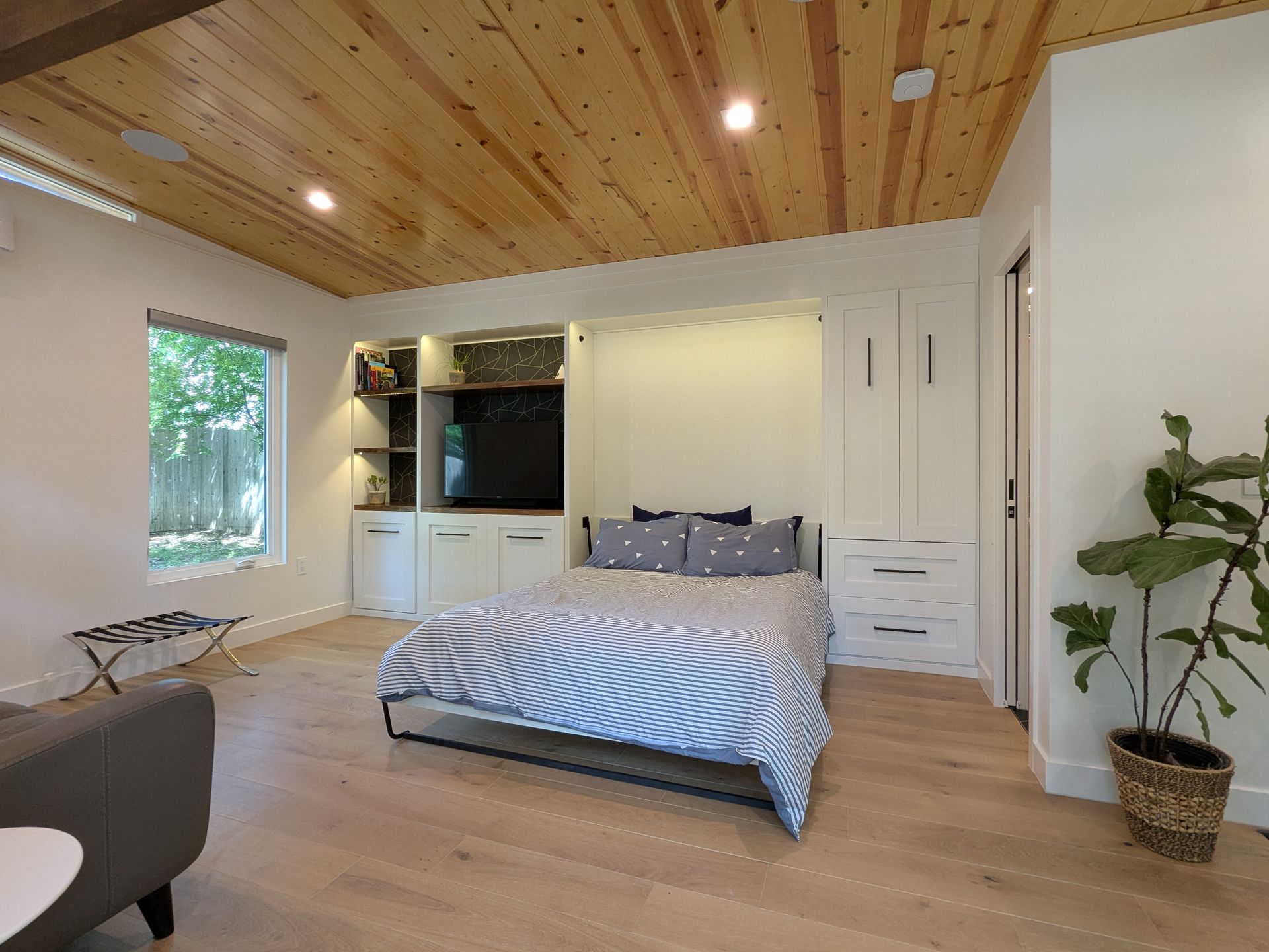 Bedroom with wood ceiling, white cabinetry, bed, TV, and potted plant.