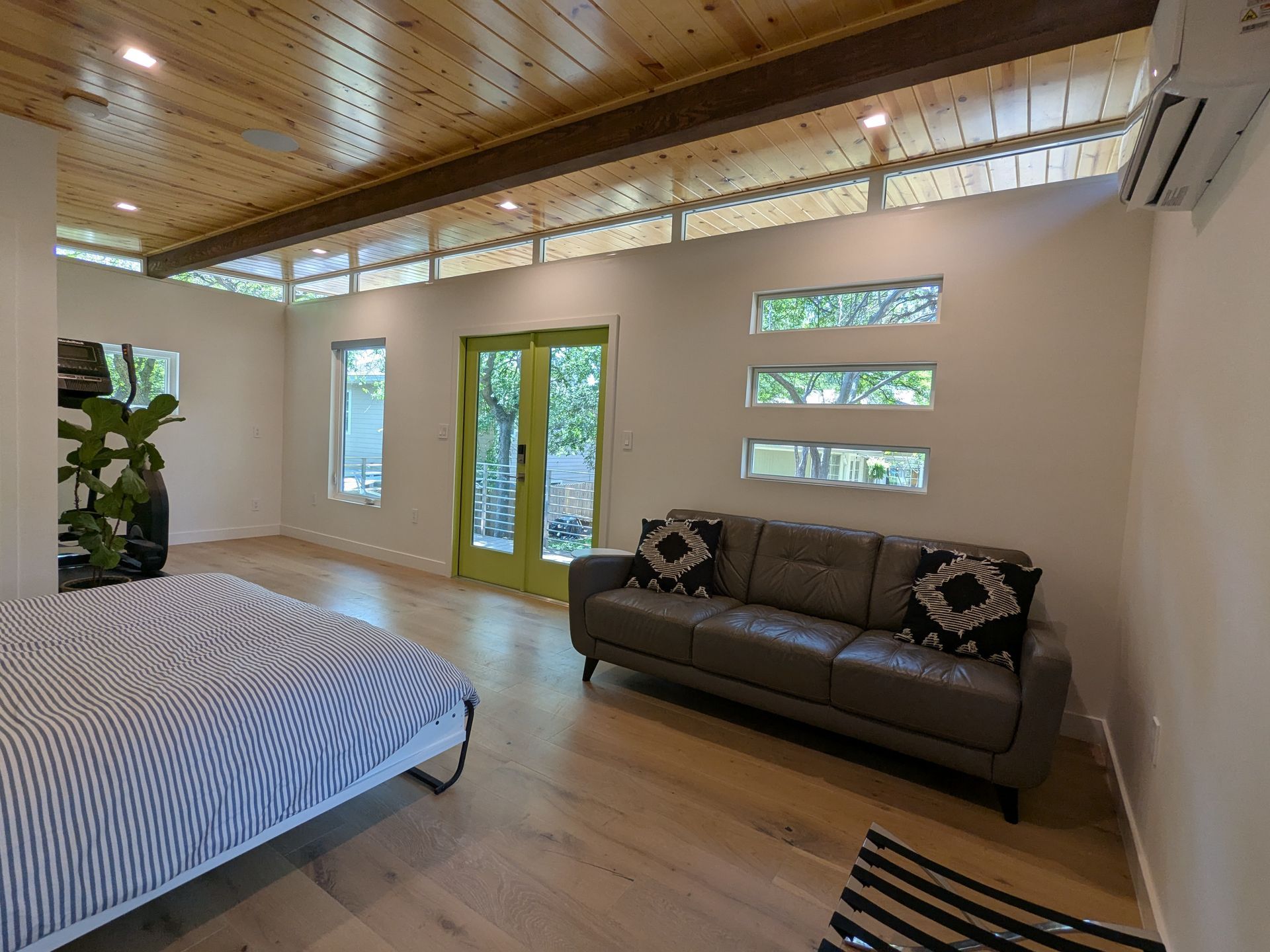 Bedroom with wooden ceiling and floor, green door, gray sofa, and bed with striped bedding.