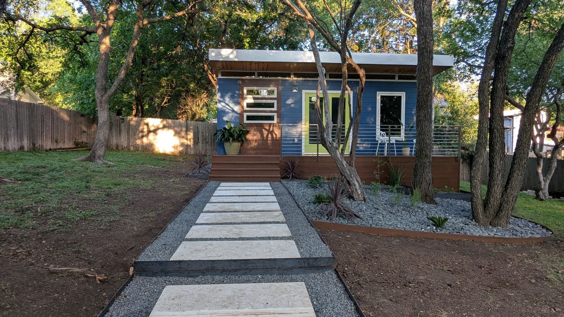 Blue tiny home with stone path, wood steps, and landscaping.