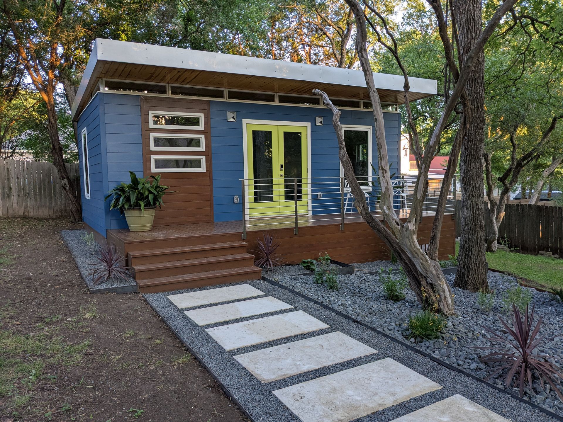 Blue modern home with lime green double doors, wooden deck, and stepping stone path.