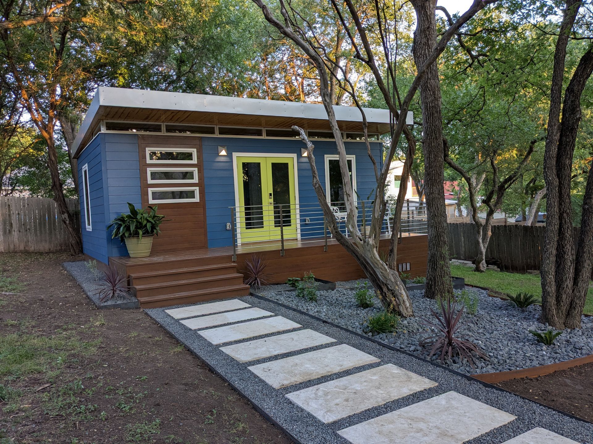 Blue tiny house with yellow doors, wooden steps, and a stone walkway.