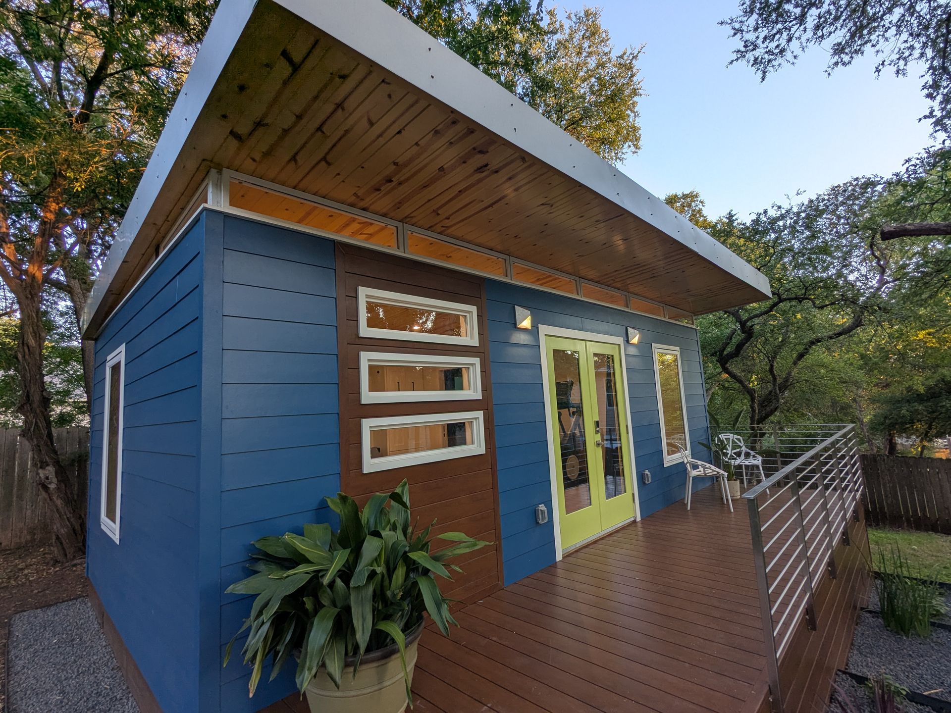 Blue and brown modern cabin with a deck, surrounded by trees.