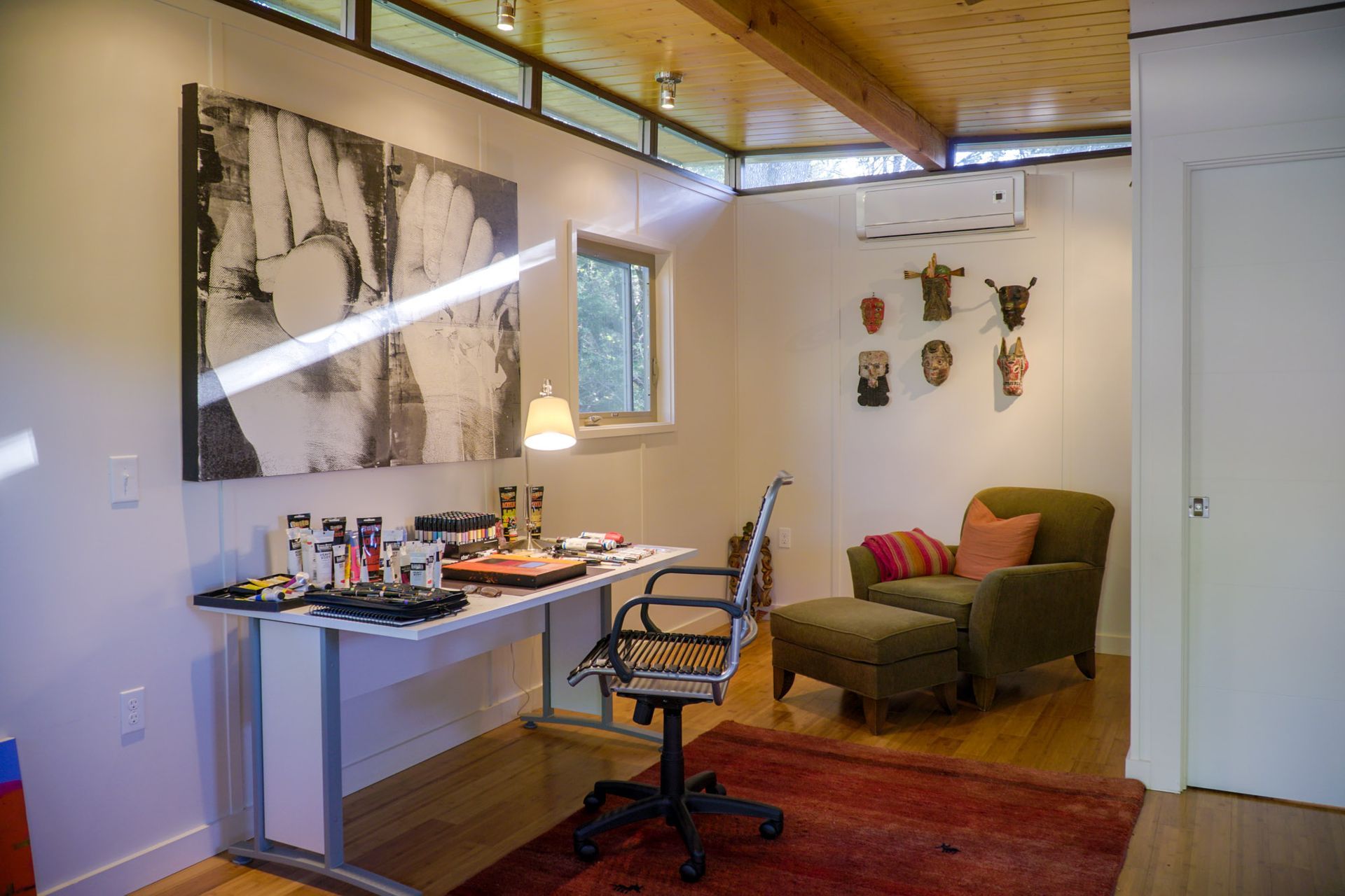 Small art studio with desk, chair, armchair, art on the walls, and wood floors.