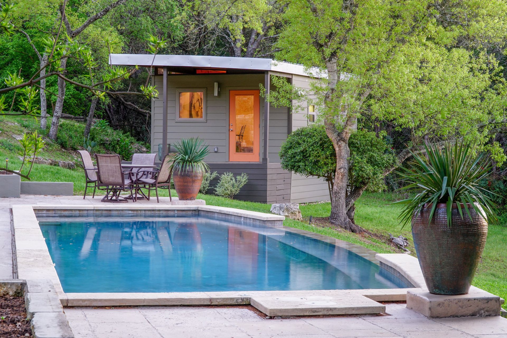 Poolside cabana with orange door, table, and chairs near a pool.