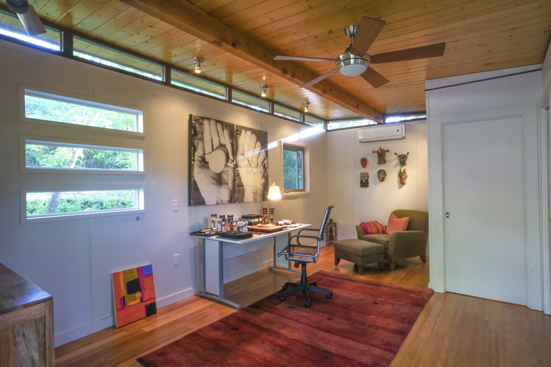 Office with desk, art, windows, red rug, and ceiling fan. Wooden ceiling and floor.