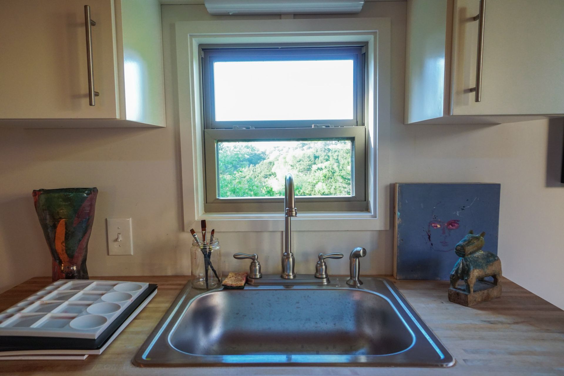 Stainless steel kitchen sink, window, and cabinets in a small kitchen.