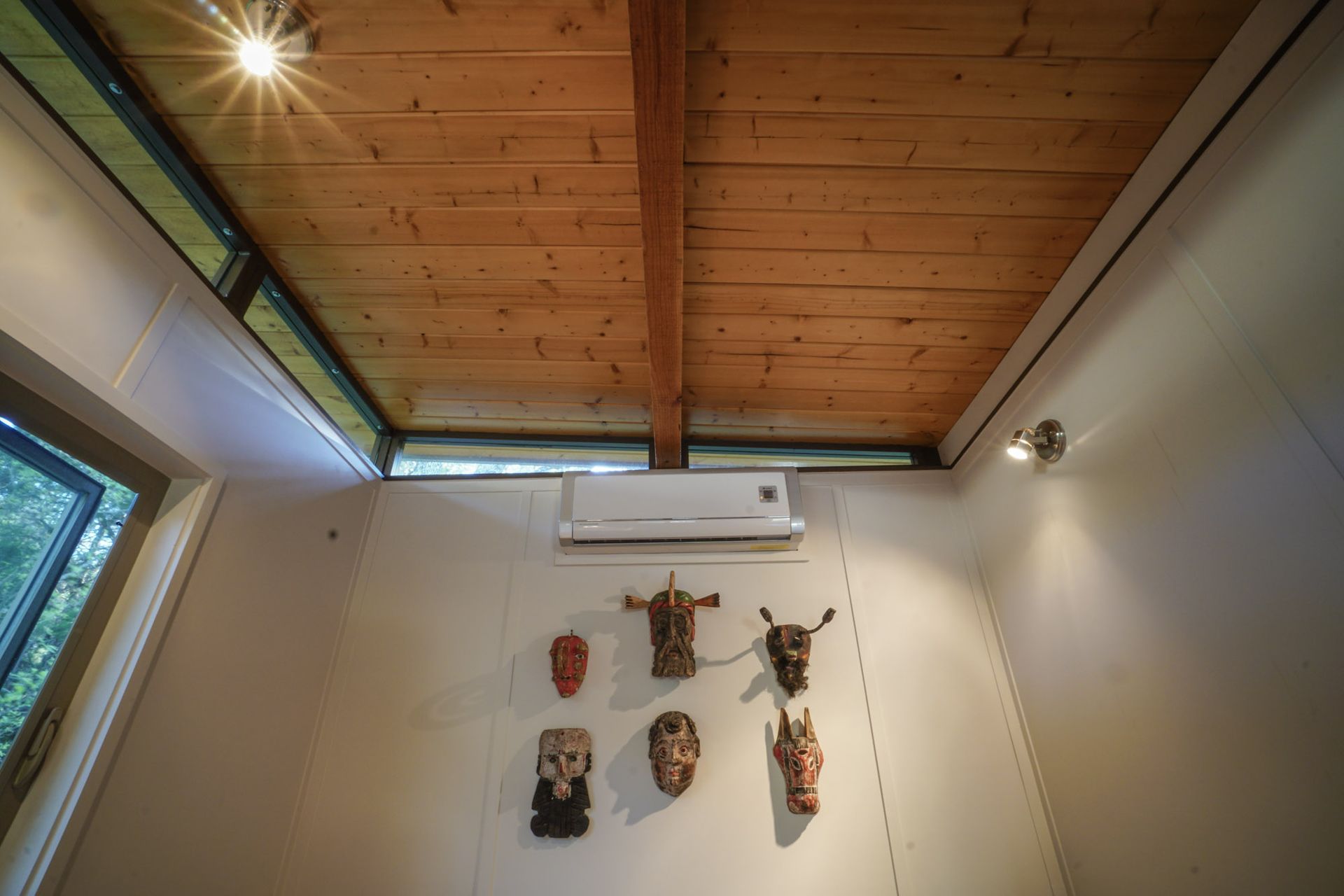 Wooden ceiling with a light fixture, wall-mounted masks, and an air conditioning unit.