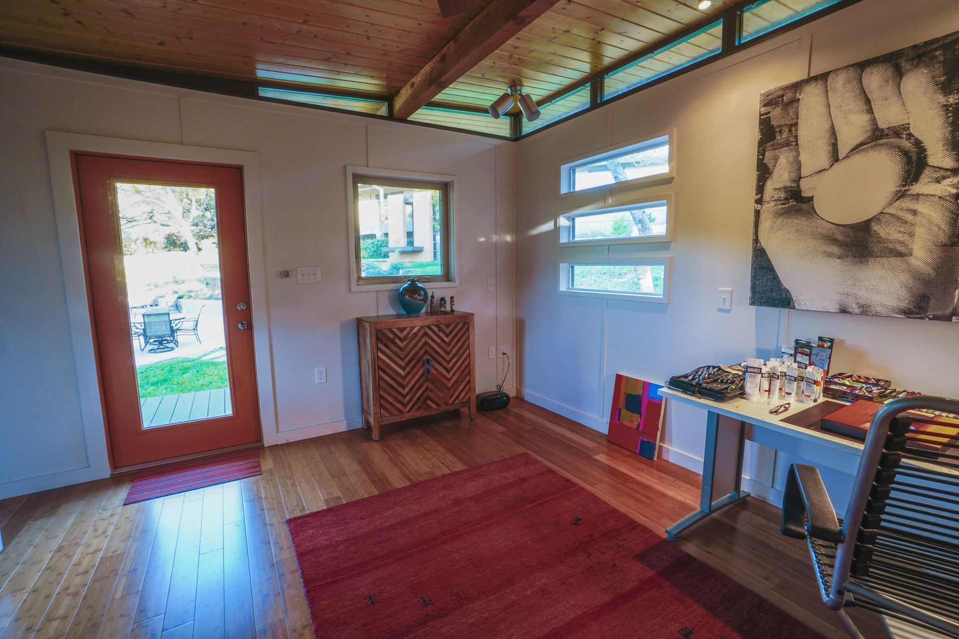 Interior room with red door, rug, wood floor, white walls, art, and desk.