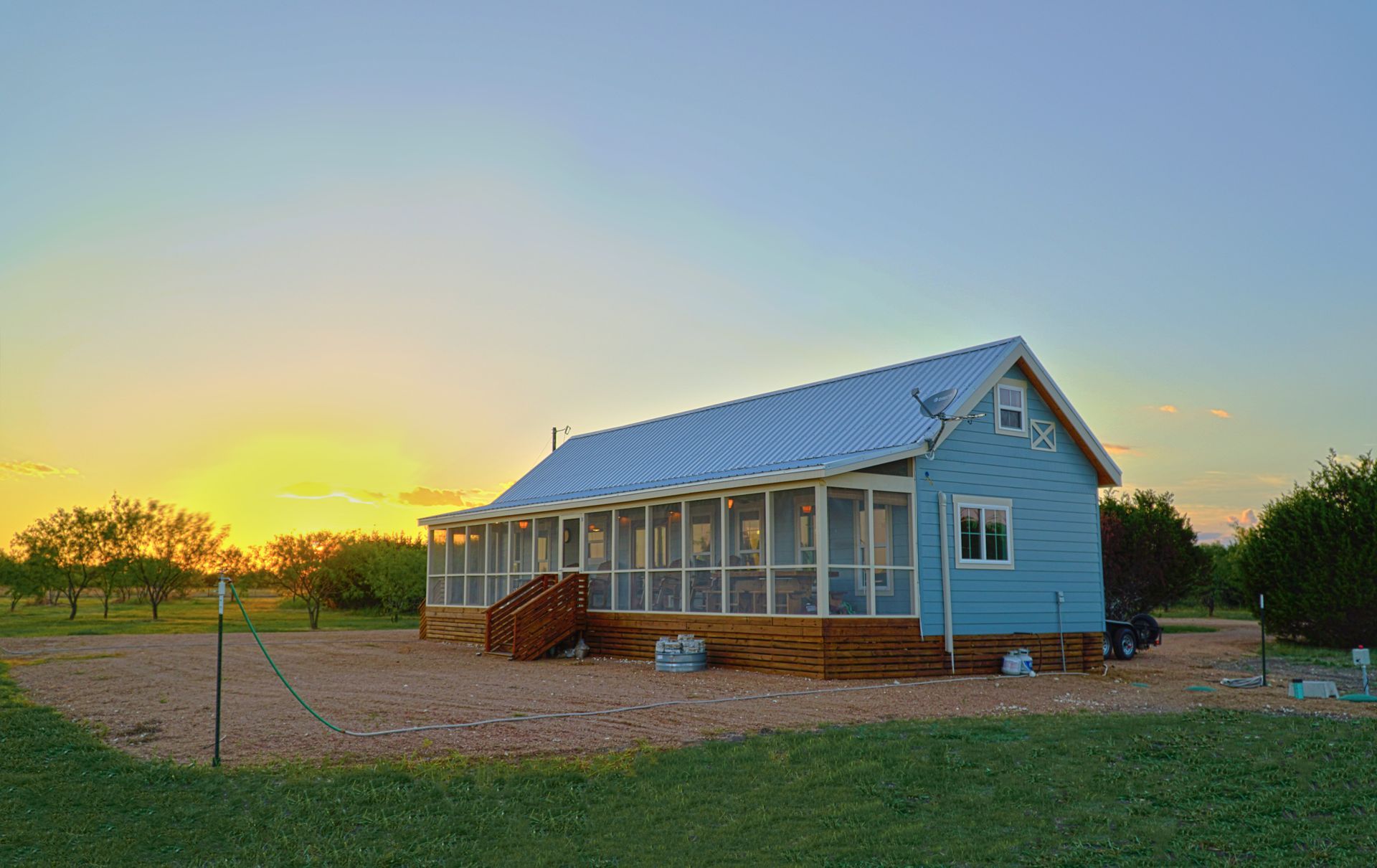 Blue house with screened porch in a field at sunset; light sky, metal roof.
