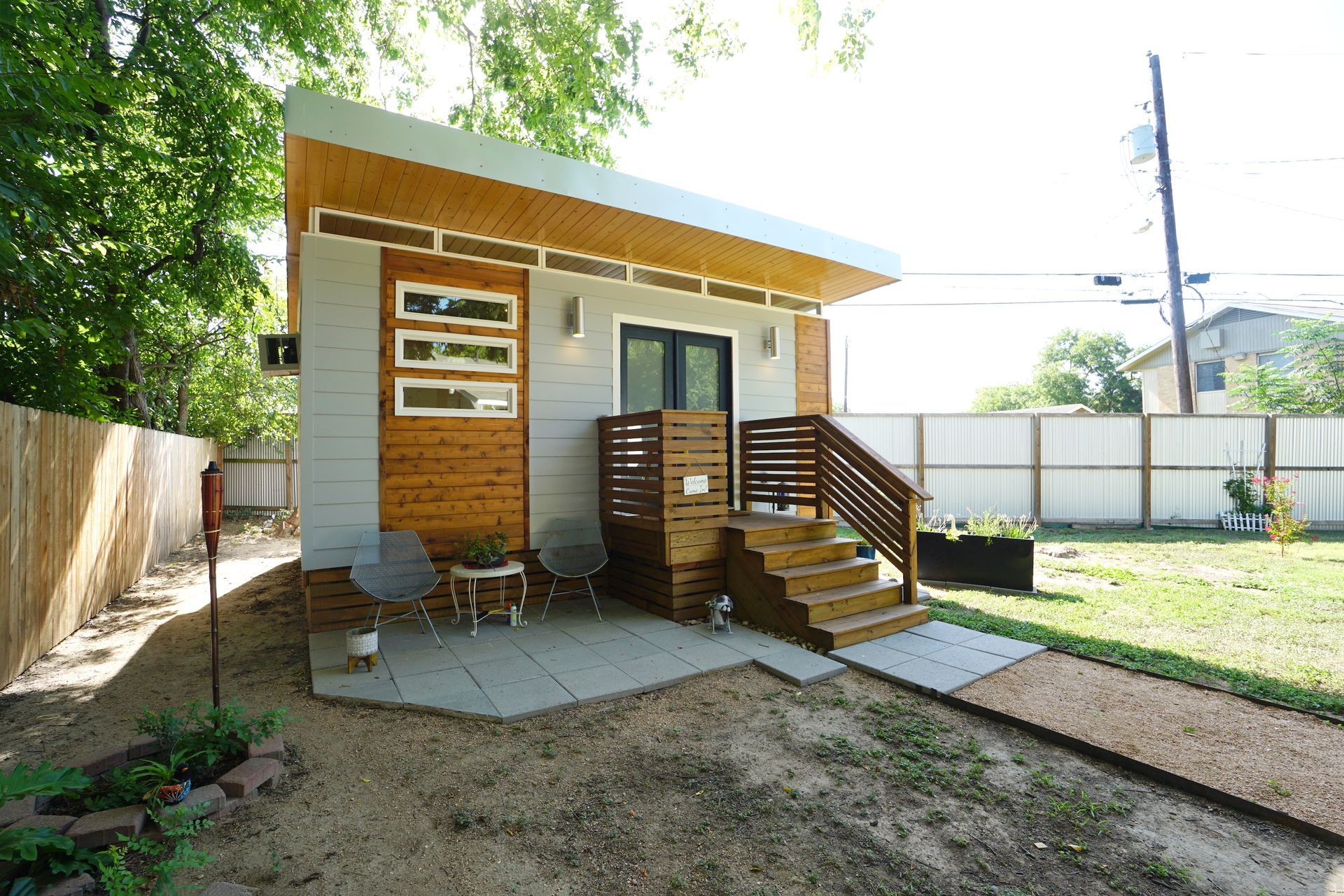 Modern tiny house with gray siding, wooden accents, and a small patio with seating.