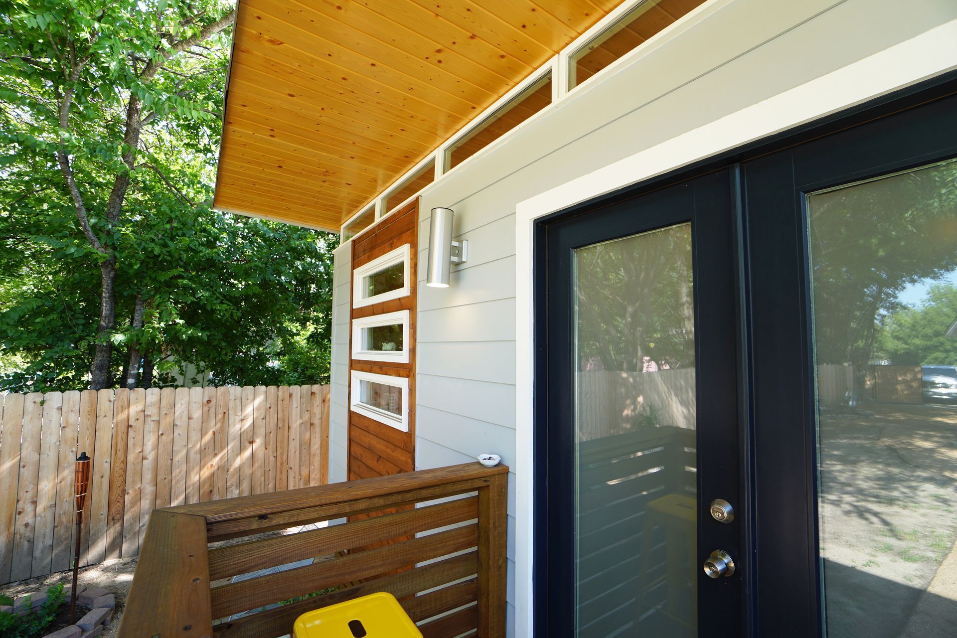 Exterior view of a modern building with a wooden deck and door. Blue door, wood paneling, and a wood ceiling.