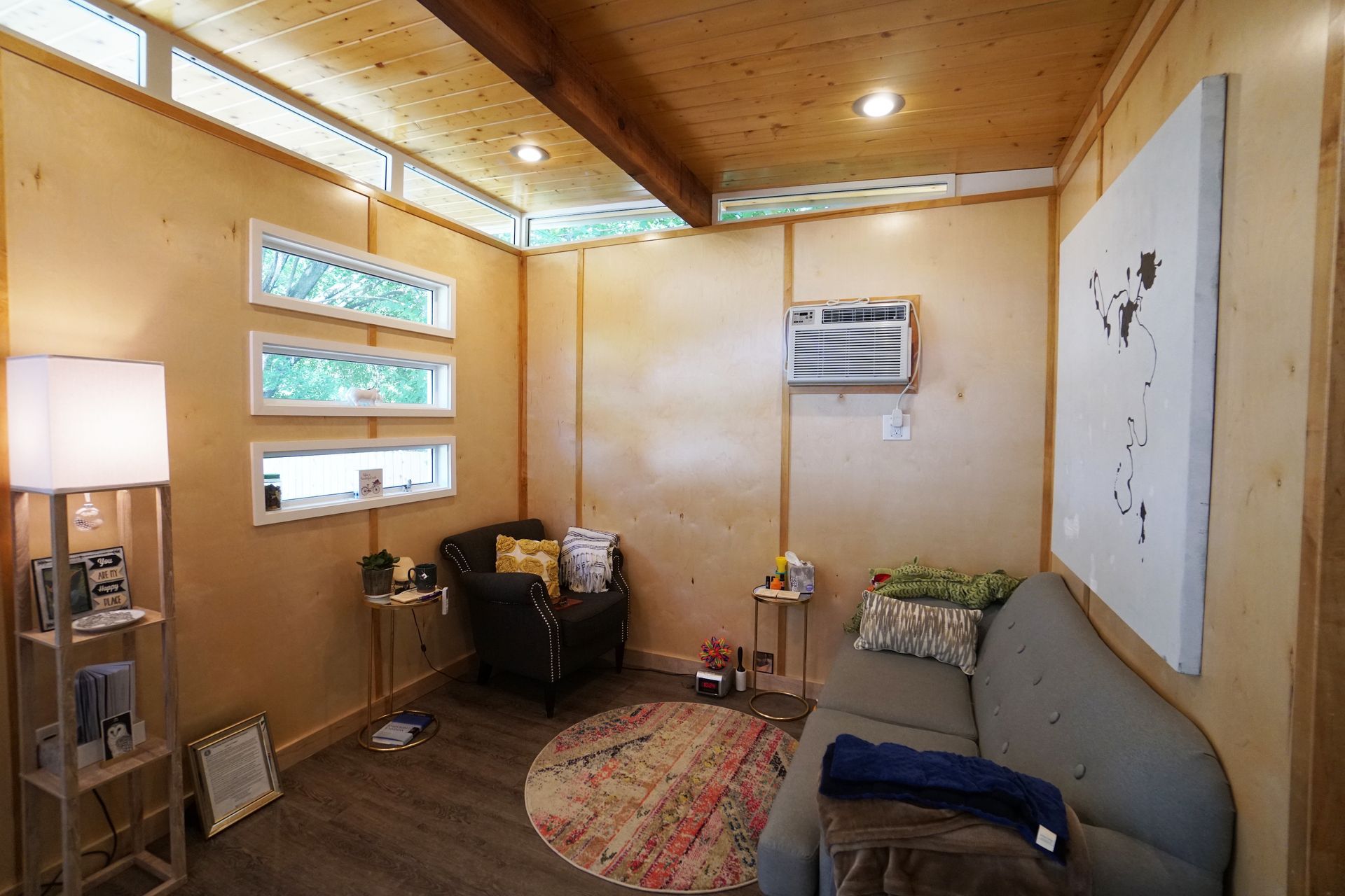 Cozy interior room with wooden walls, small windows, a couch, armchair, rug, and artwork.