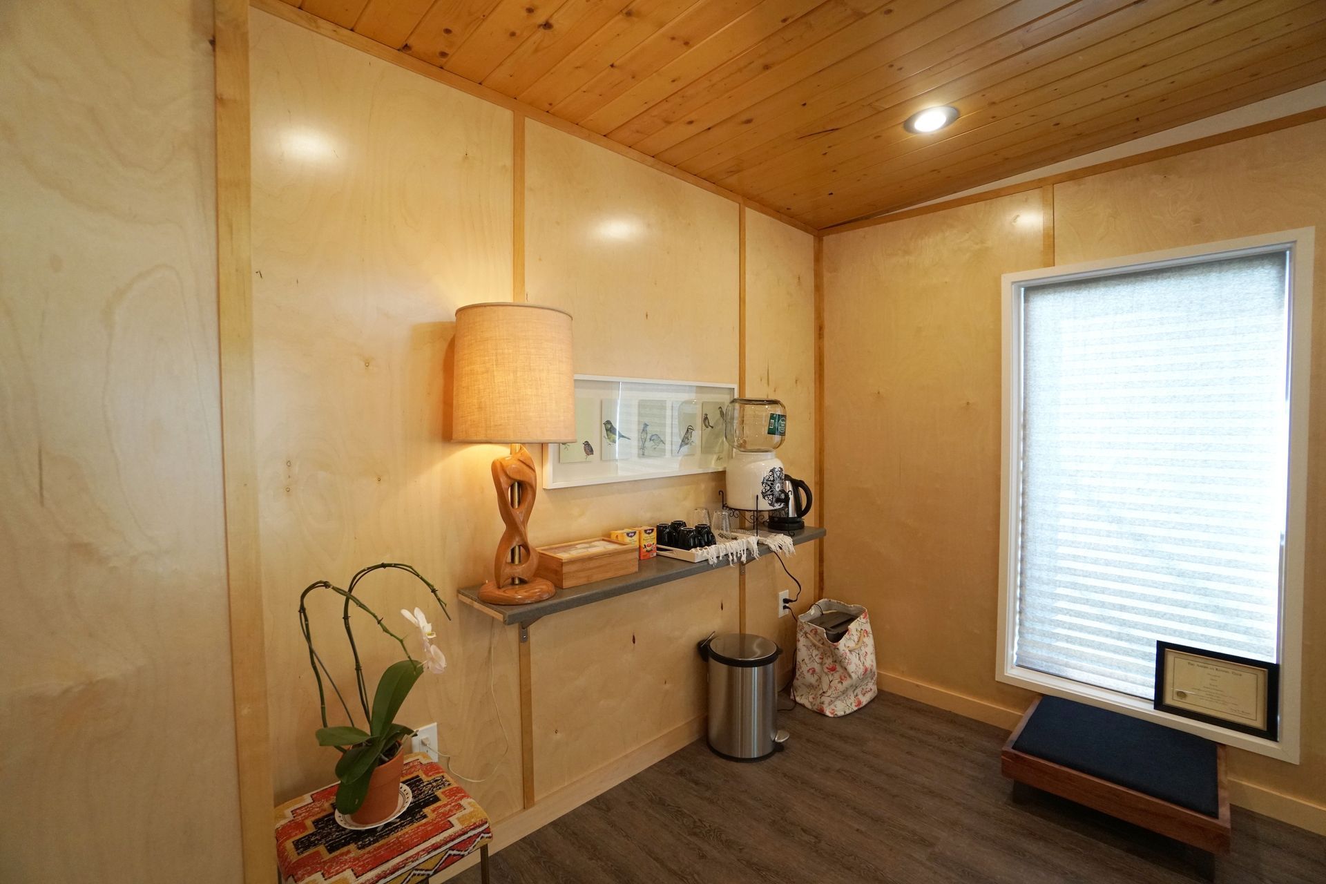 Small room with light wood paneling, a lamp, a window with blinds, and a small counter with appliances.