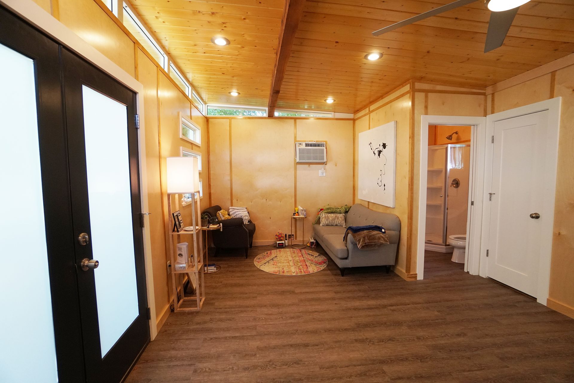Interior of a small living space with wood paneling, gray sofa, and a black door.