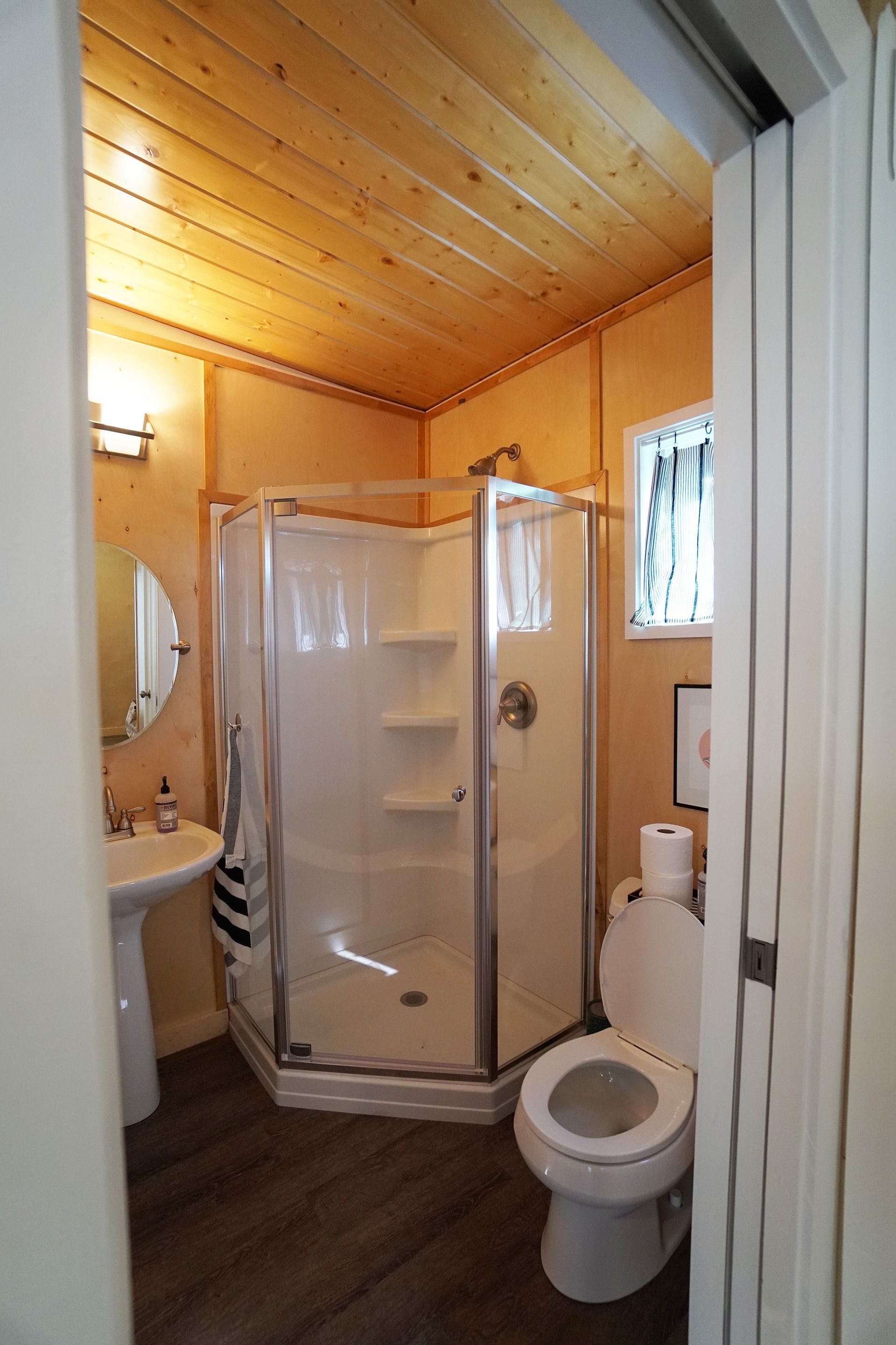 Small bathroom with a shower, toilet, and pedestal sink; wooden ceiling.