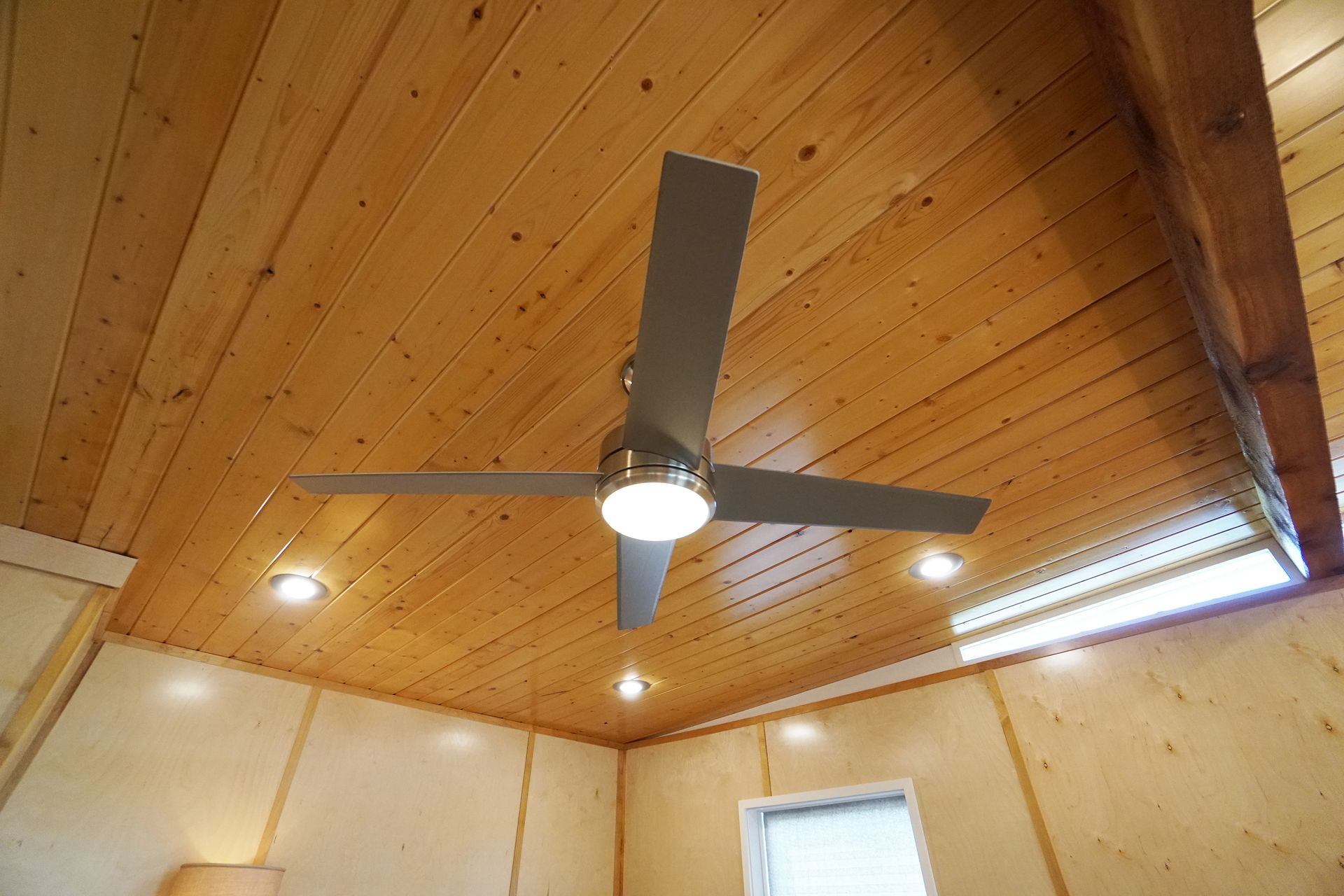 Ceiling fan with light on a wood-paneled ceiling, recessed lighting.