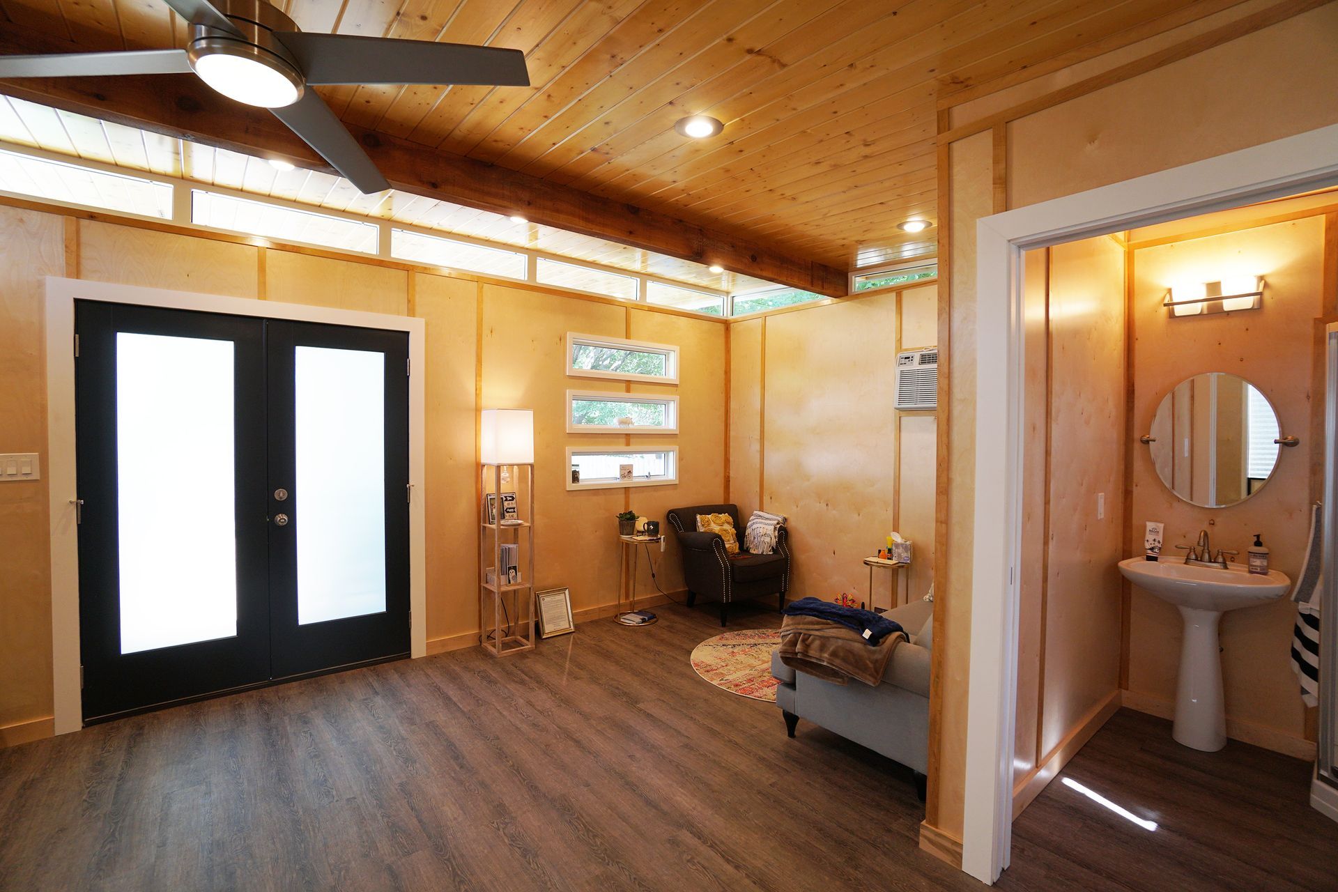 Interior of a small room with wood paneling, dark gray floor, a bathroom, and a black double door.