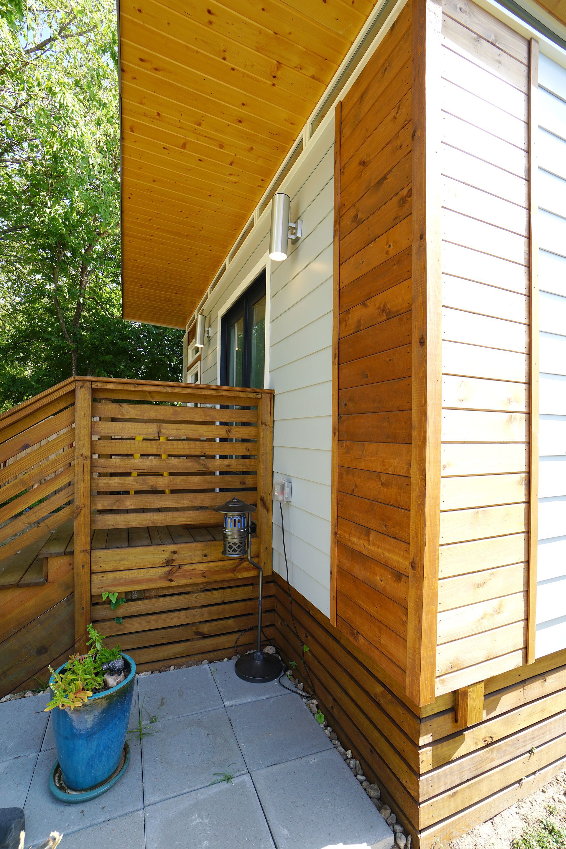 Exterior view of a modern building with wooden accents, a small patio, and a blue potted plant.